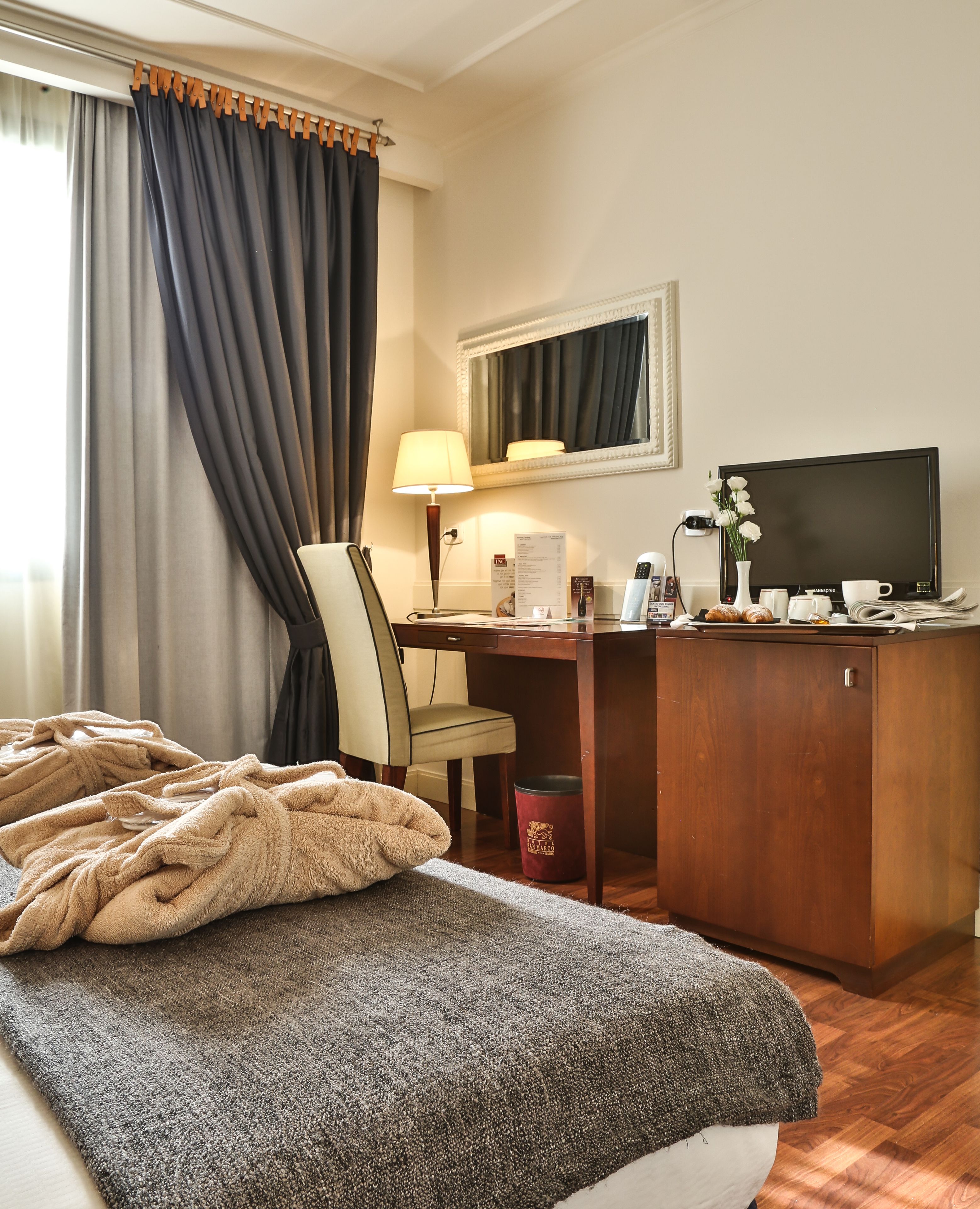 Hotelkamer met een bed, een bureau, een lamp, een televisie en een tafeltje met een bloemenvaas.