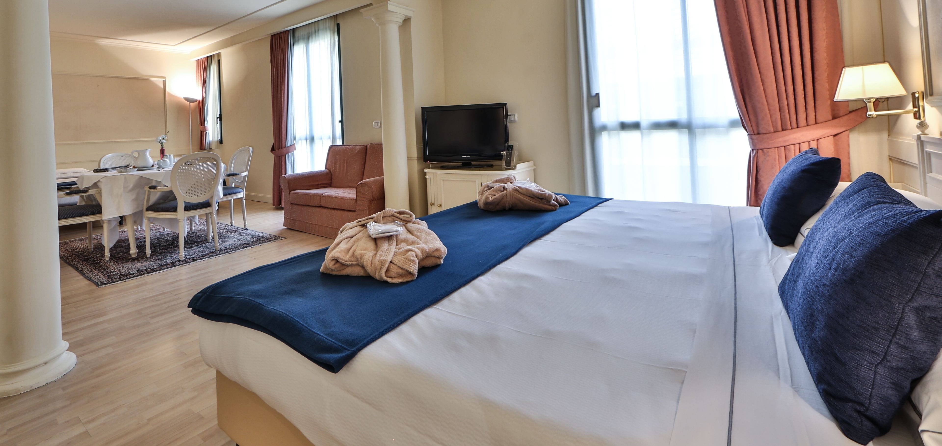 Une chambre d’hôtel comprenant un lit, un bureau avec des chaises, une télévision et une fenêtre avec des rideaux.