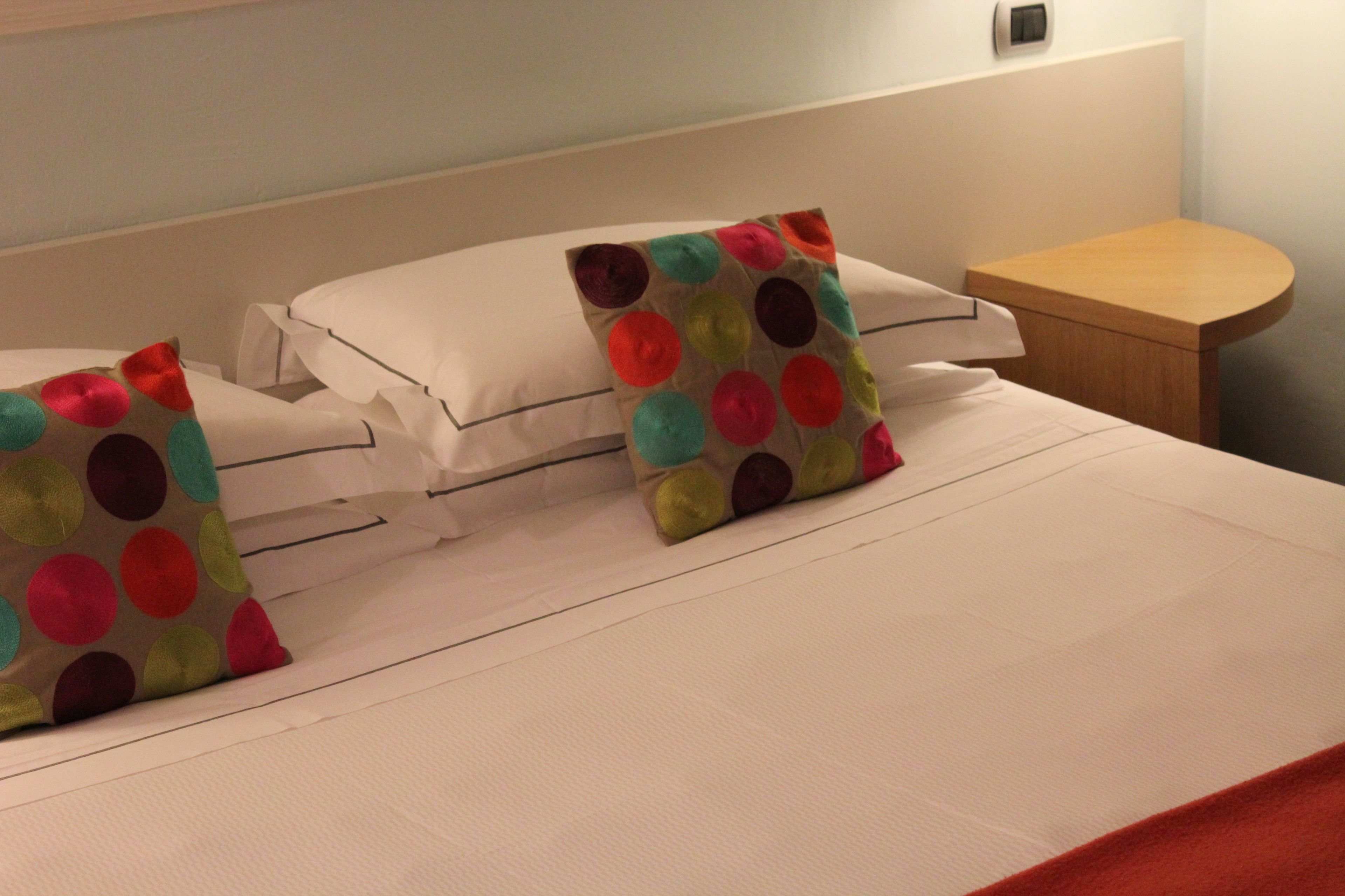 Un lit bien fait, avec des draps blancs et des coussins à pois colorés.