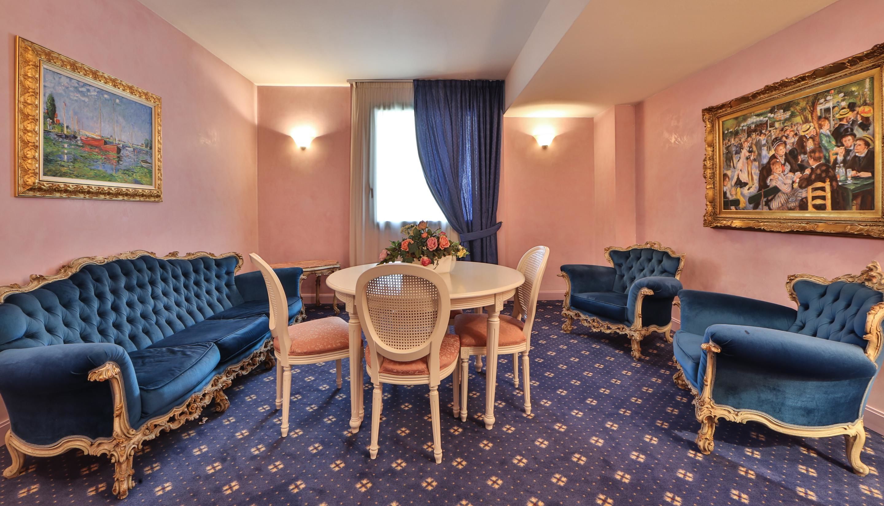 Een kamer met een ronde tafel, vier blauwe bekleden stoelen, een witte stoel en een blauw kamerbreed tapijt.