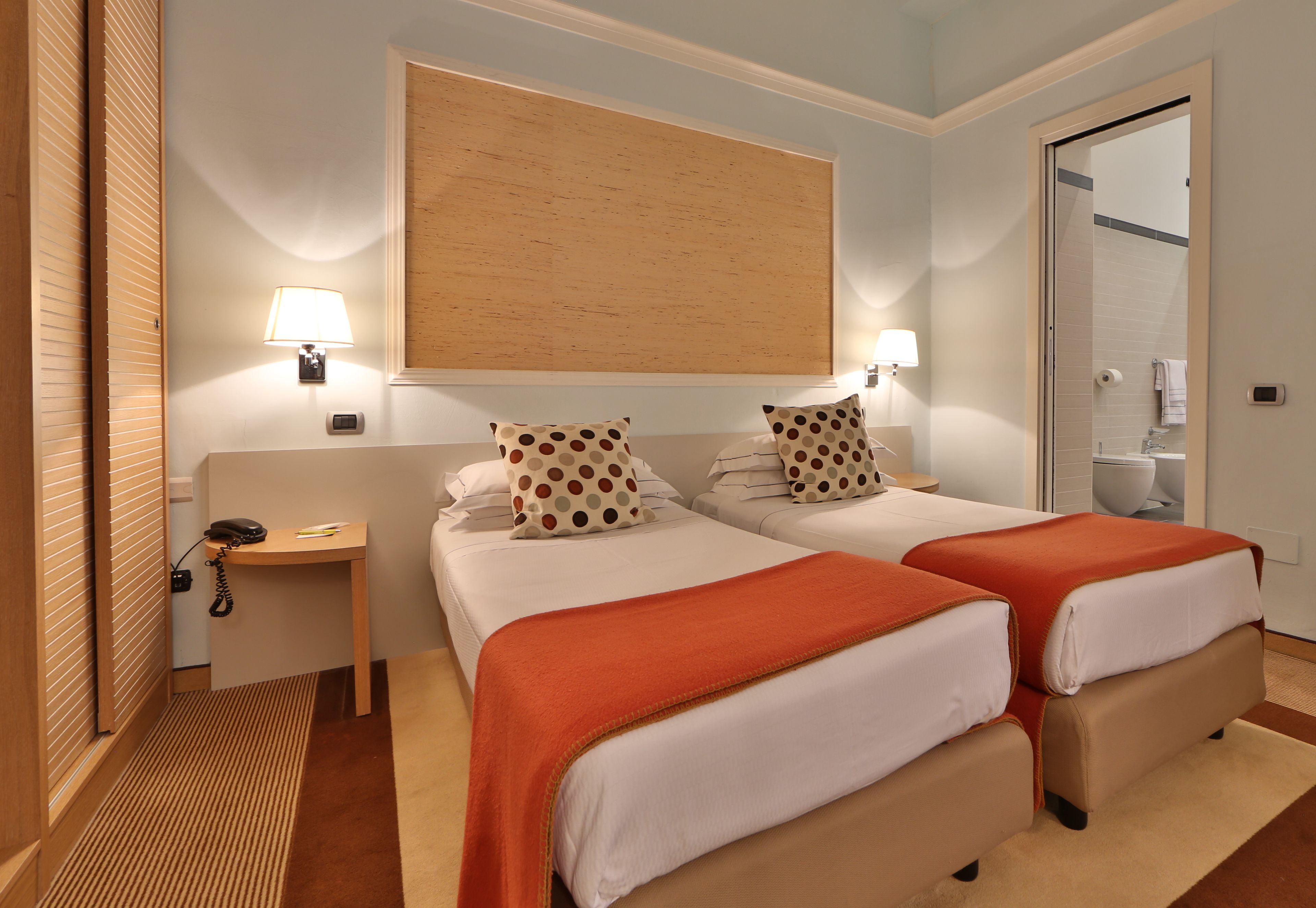 Habitación de hotel con dos camas, un cabecero de madera, un espejo grande y un baño visible a través de una puerta abierta.