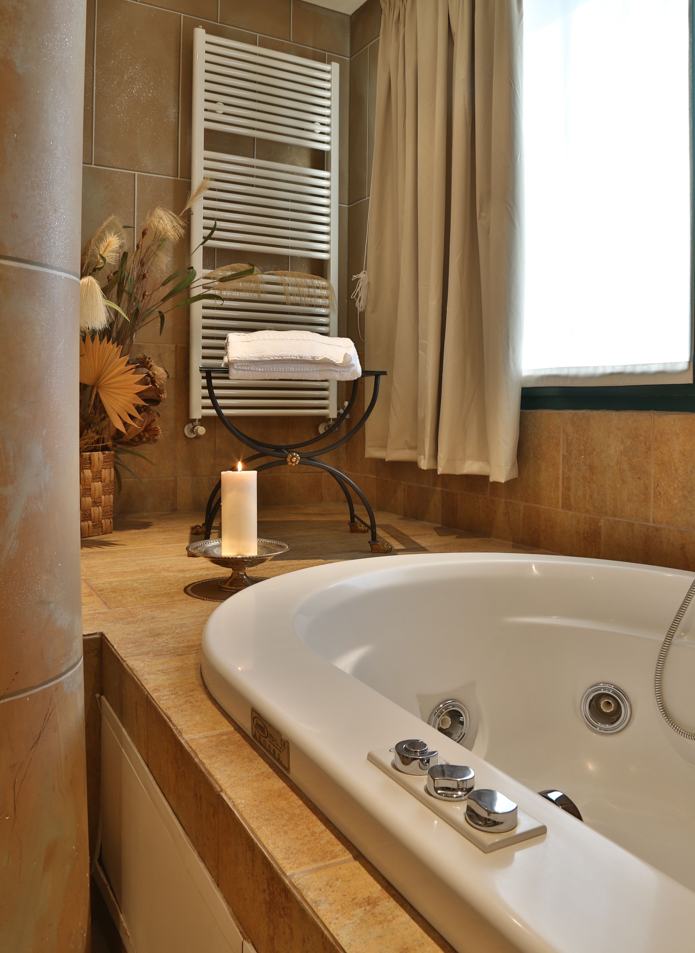 A bathroom with a bathtub, a towel rack, a candle, and decorative plants.