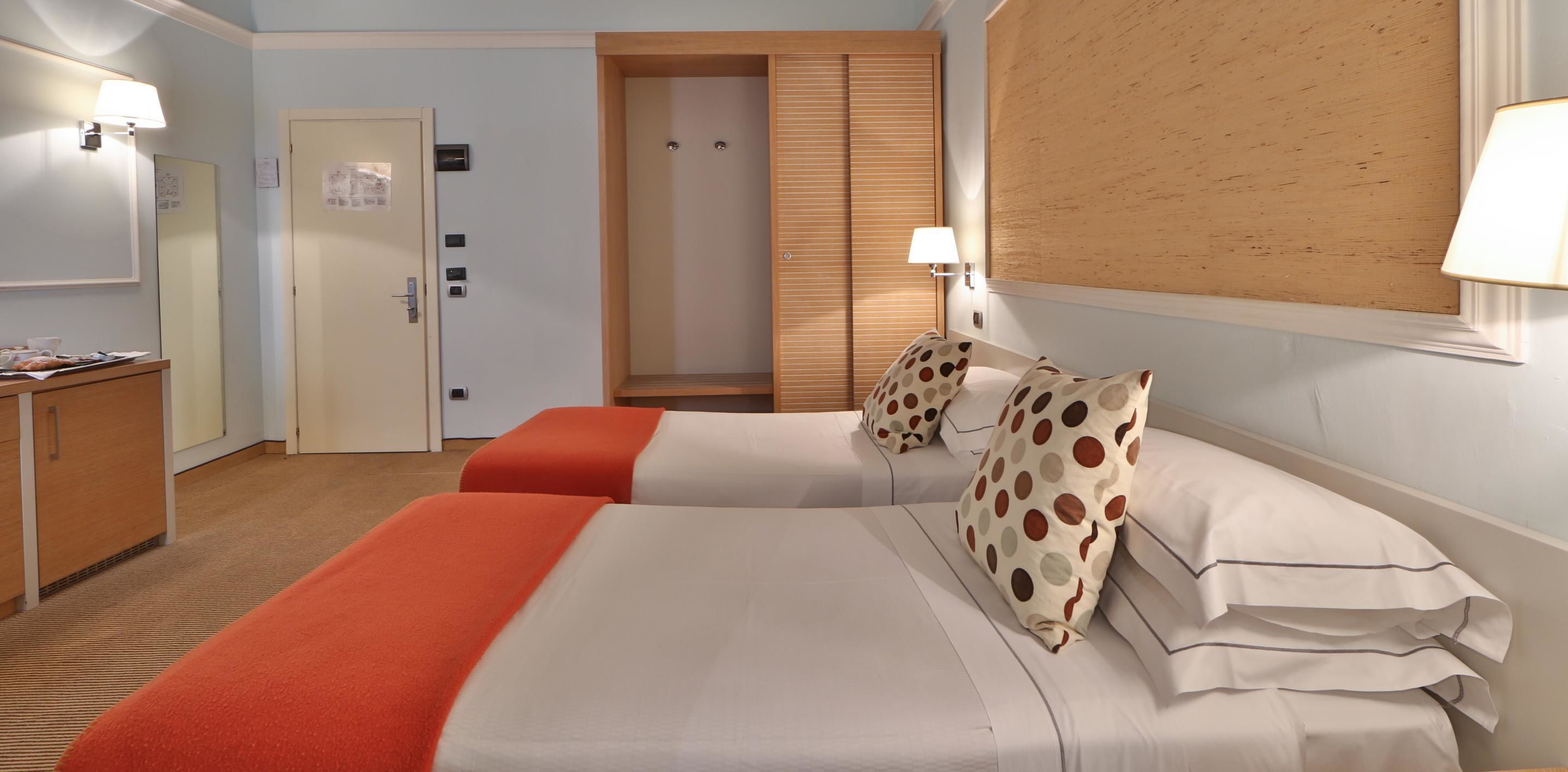 Ein Hotelzimmer mit zwei Betten, einem Holzschrank, einem Schreibtisch mit Lampe und einem Spiegel.