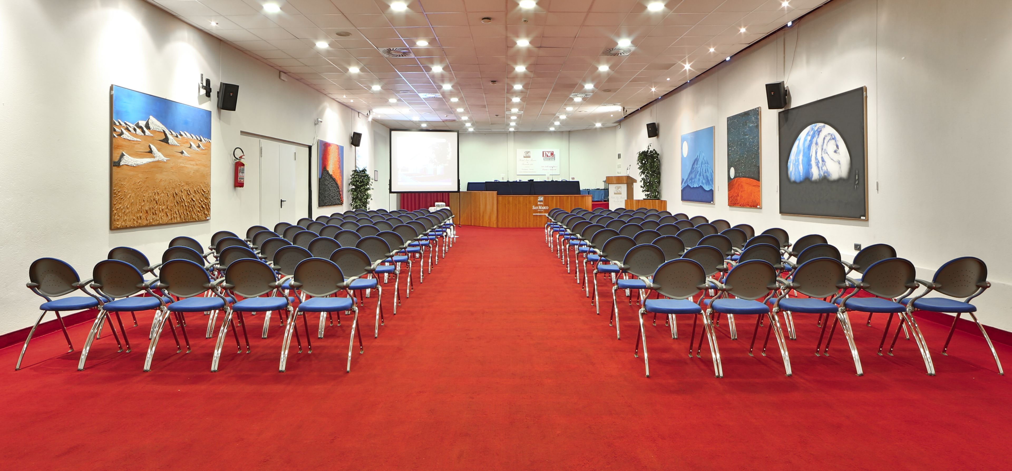 Un salón de conferencias con filas de sillas, un atril y una pantalla al frente.