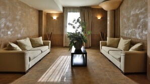 A spacious room with two sofas facing each other, a central table with a plant, and a large window with curtains. - Hotel San Marco & Formula Club (Noceto)