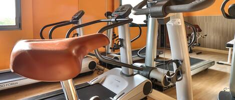 Una bicicleta estática con panel de control, una cinta de correr y un espejo que refleja la sala.