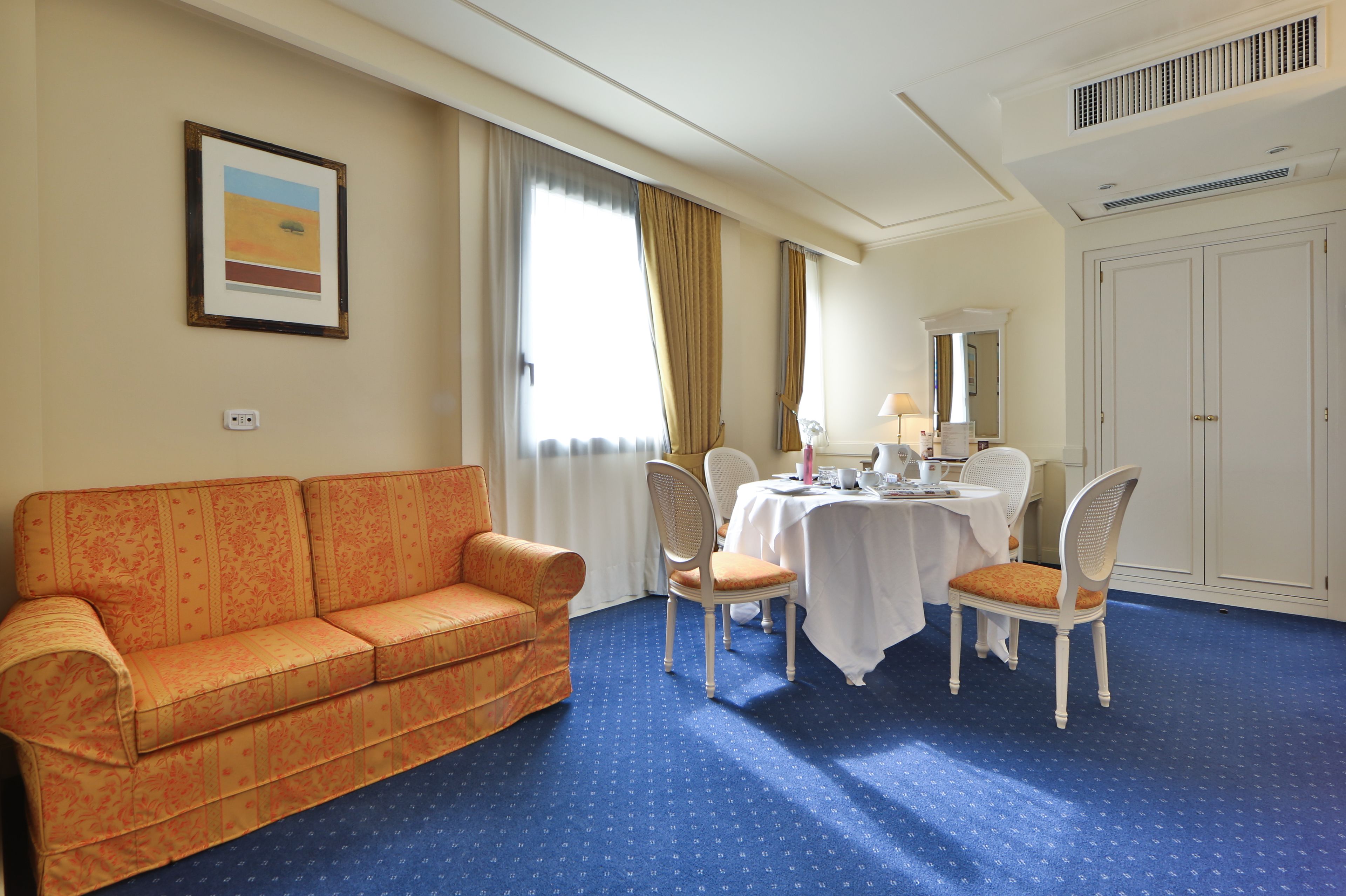 A hotel room with a sofa, dining table, chairs, and a large mirror.