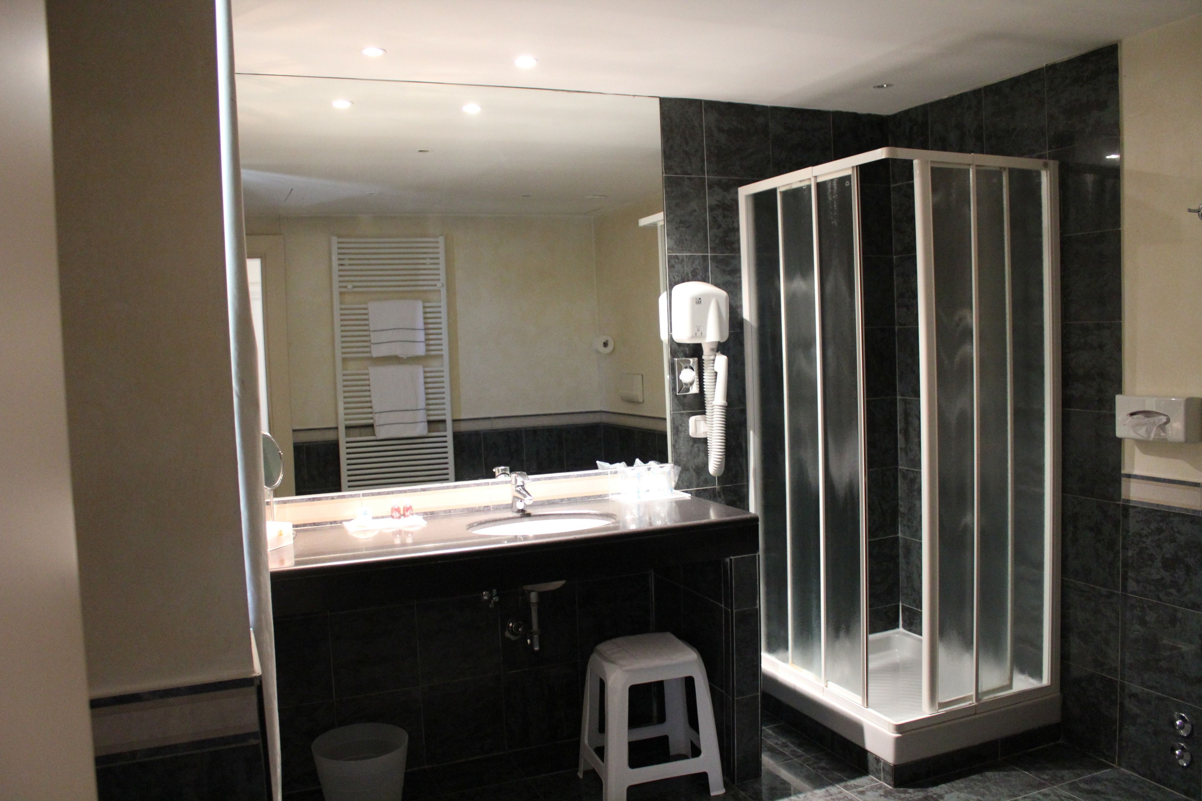 Un baño moderno con cabina de ducha de vidrio, un lavamanos con espejo y un taburete blanco.
