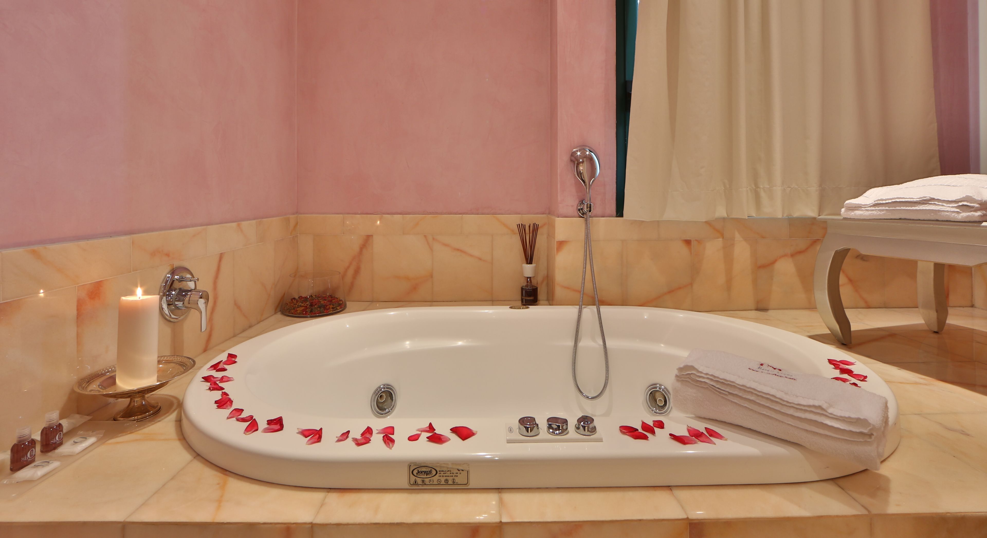 Ein Badezimmer mit einer großen Badewanne, einem Waschtisch mit Spiegel, einem Handtuchhalter und einer Kerze am Rand.