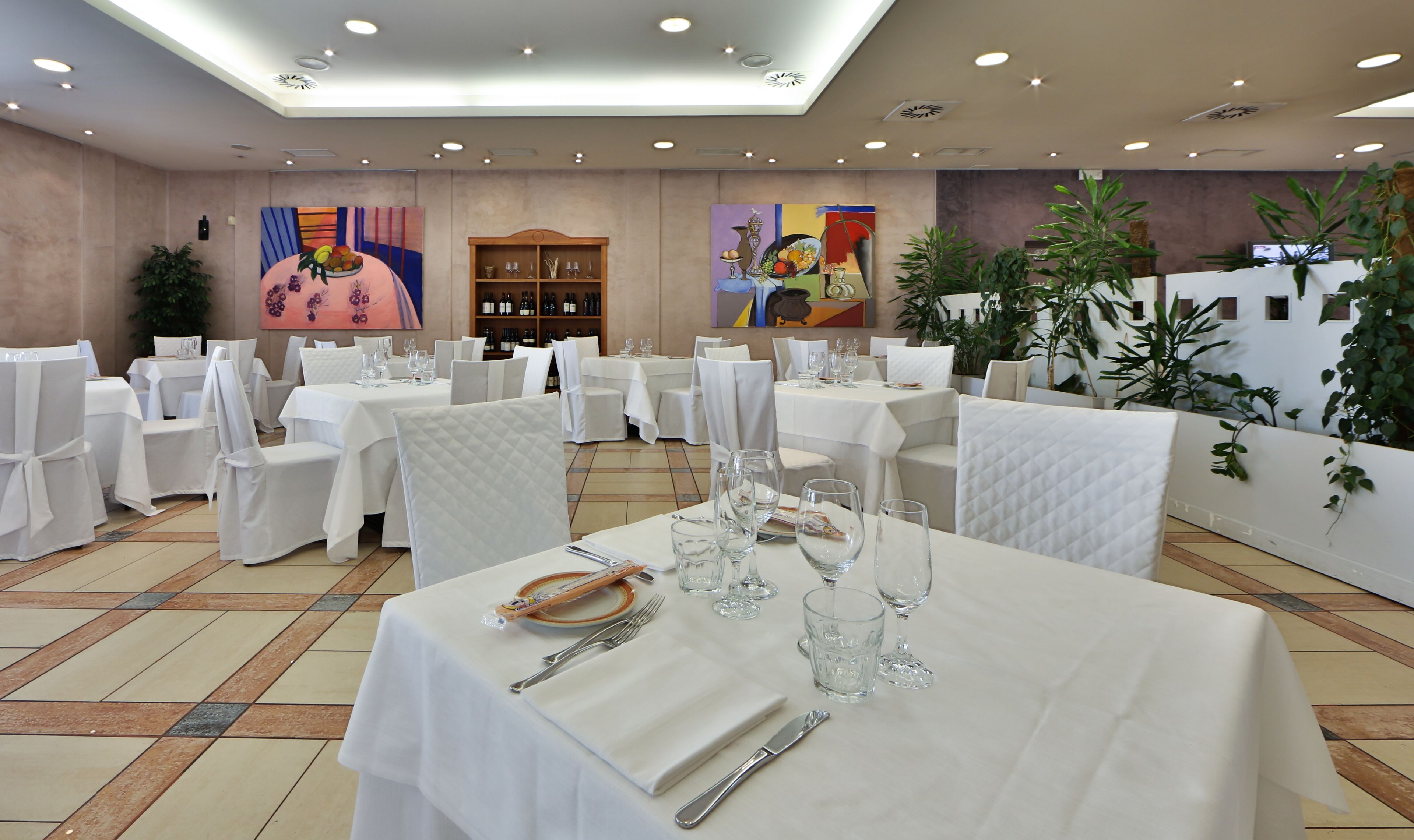 A dining area with tables set for a meal, chairs with white covers, and a ceiling with recessed lighting.