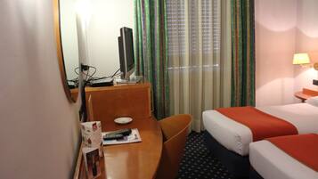 A hotel room with a desk, a television, two beds, and a window with curtains.