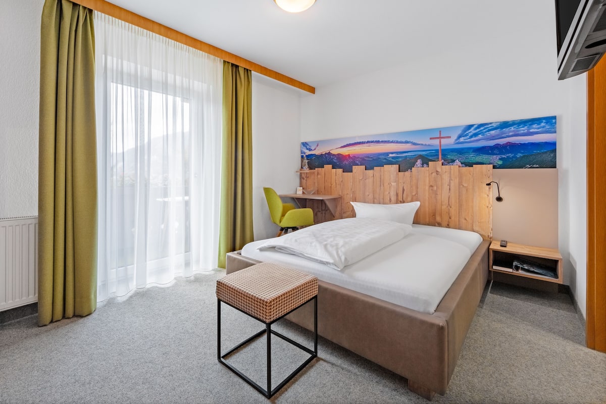 A modern hotel room with a bed, a small table, a chair, and a painting on the wall.