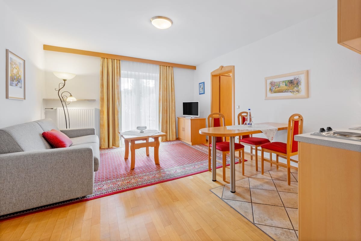 A modern living room with a sofa, a dining table with chairs, a TV, and a kitchen area.