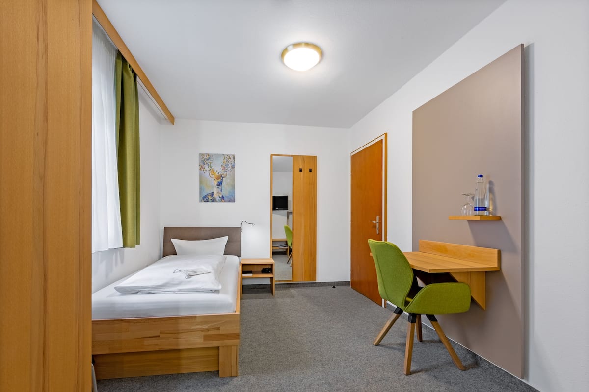 A compact hotel room with a single bed, a desk, a chair, and a small table.
