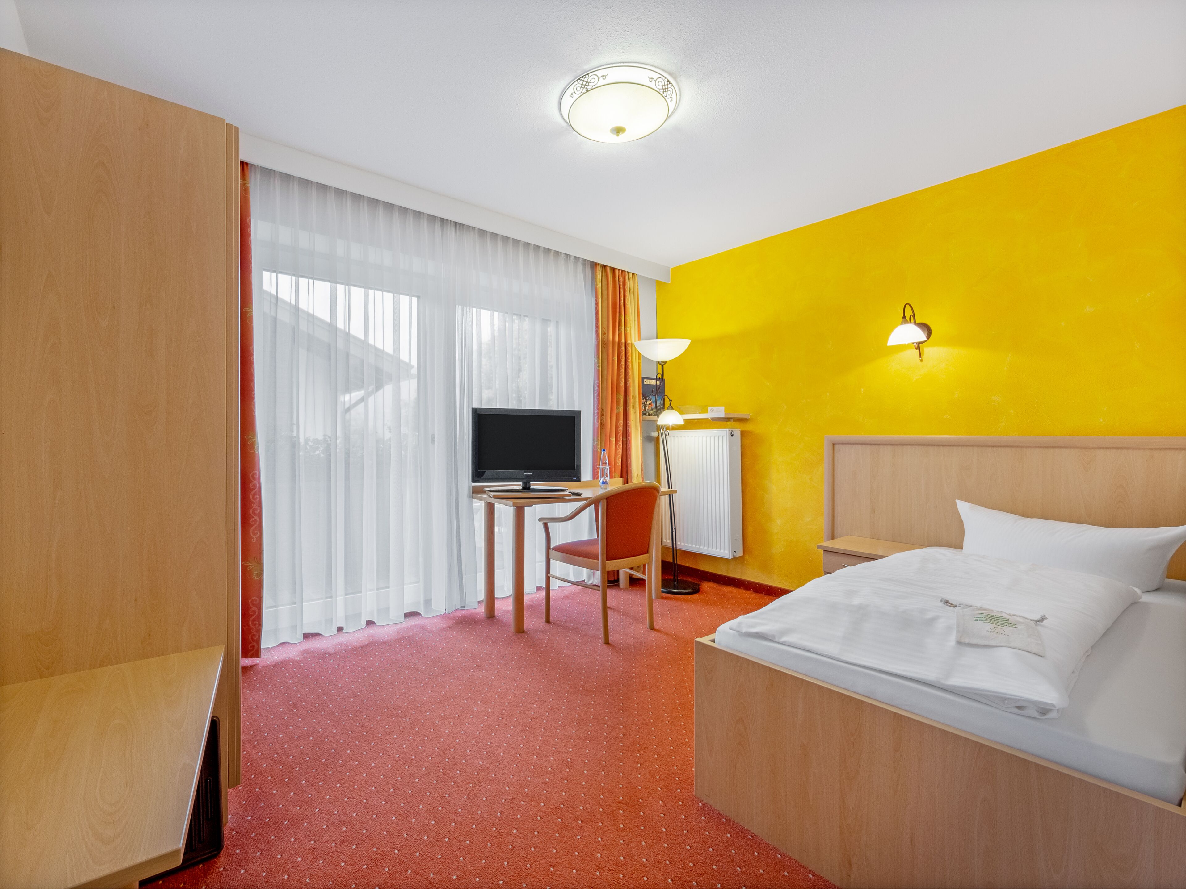 Habitació d'hotel amb un llit, escriptori amb ordinador, cadira i televisió.