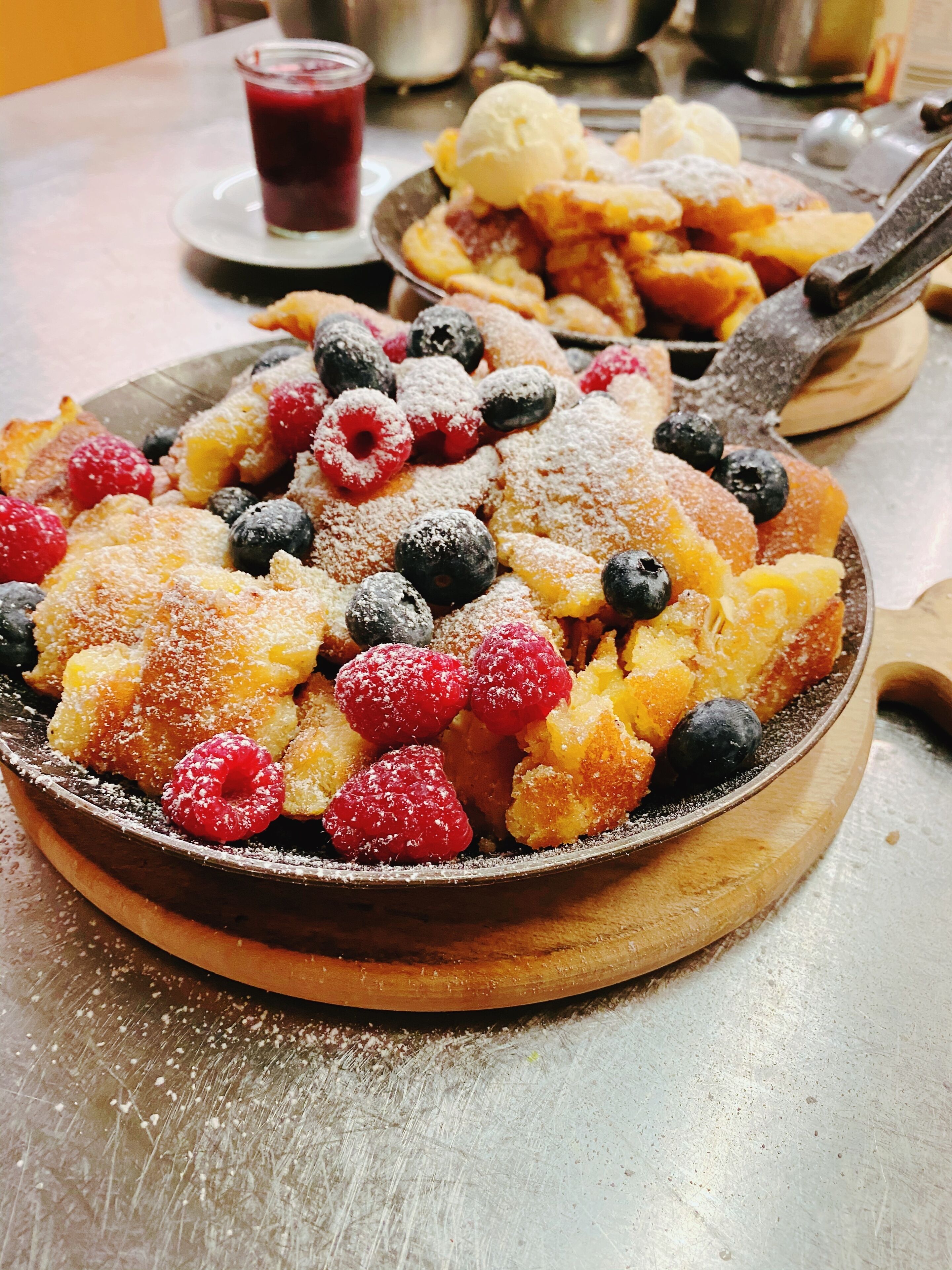 Een ontbijt bord met pannenkoeken, bosbessen, frambozen en een bolletje ijs.