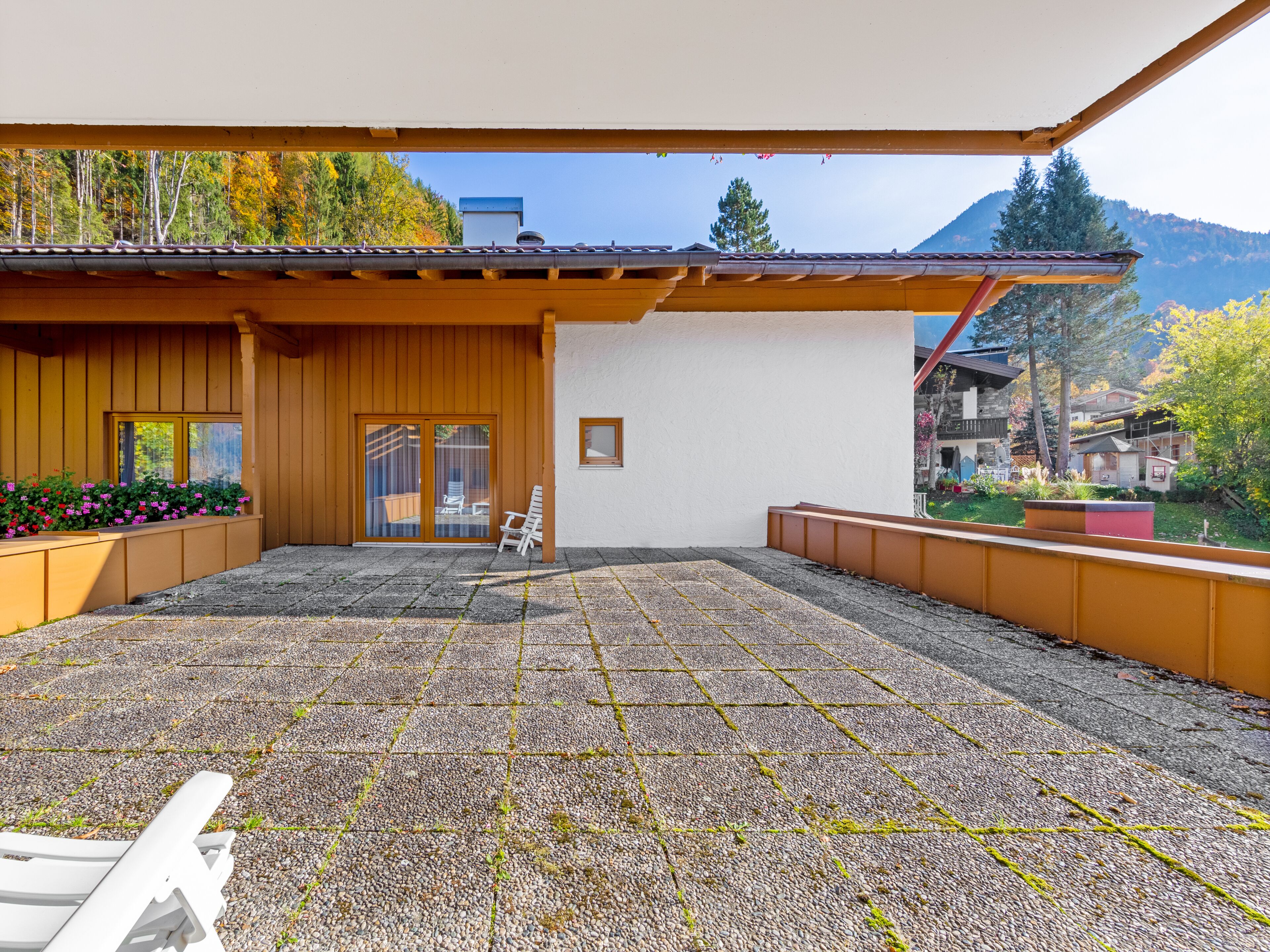 Un patio cubierto con piso de grava, una terraza de madera y una silla blanca.
