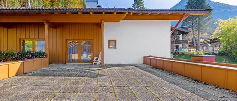 A covered patio with a gravel floor, wooden deck, and a white chair.