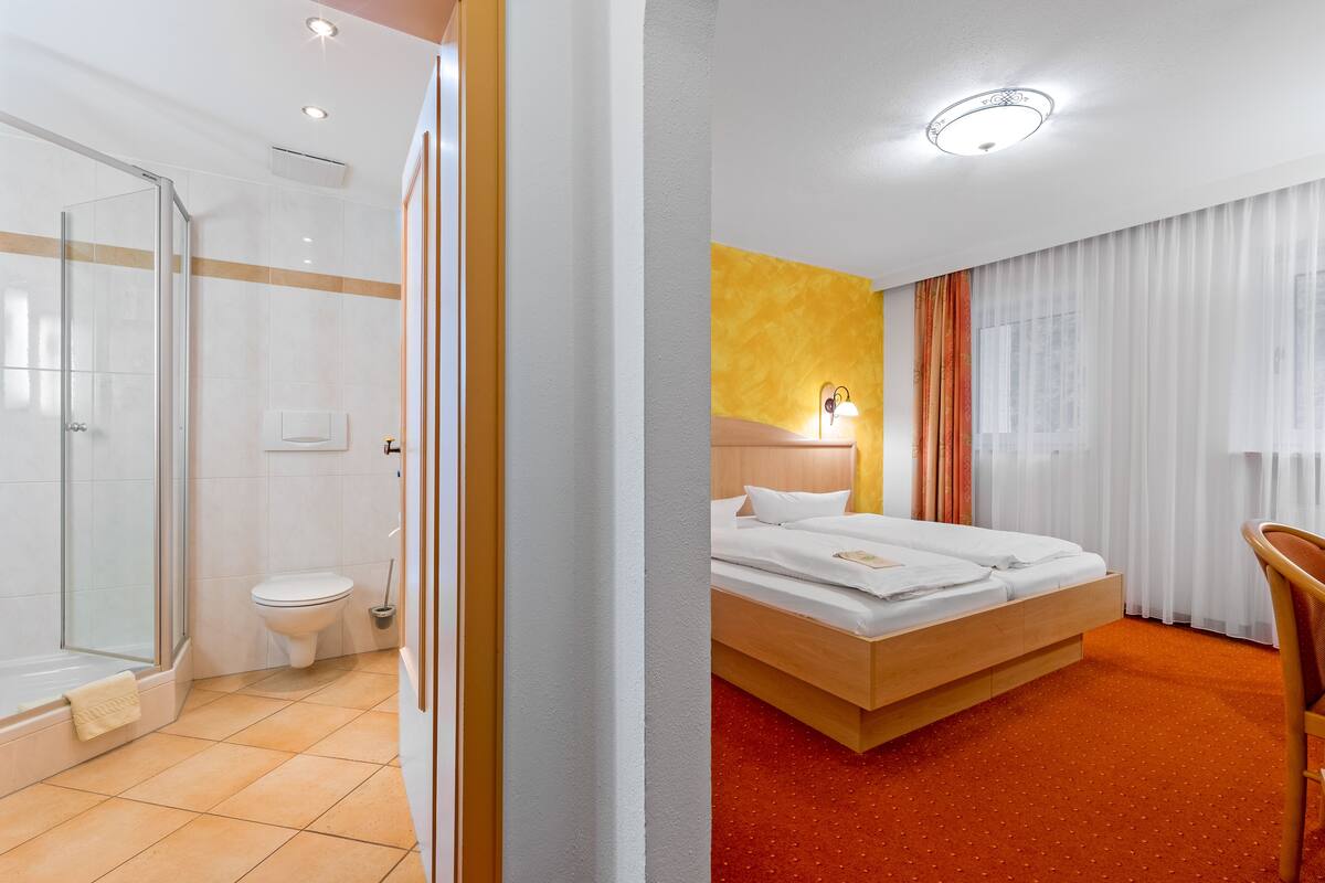 A hotel room with a shower, toilet, bed, and a chair.