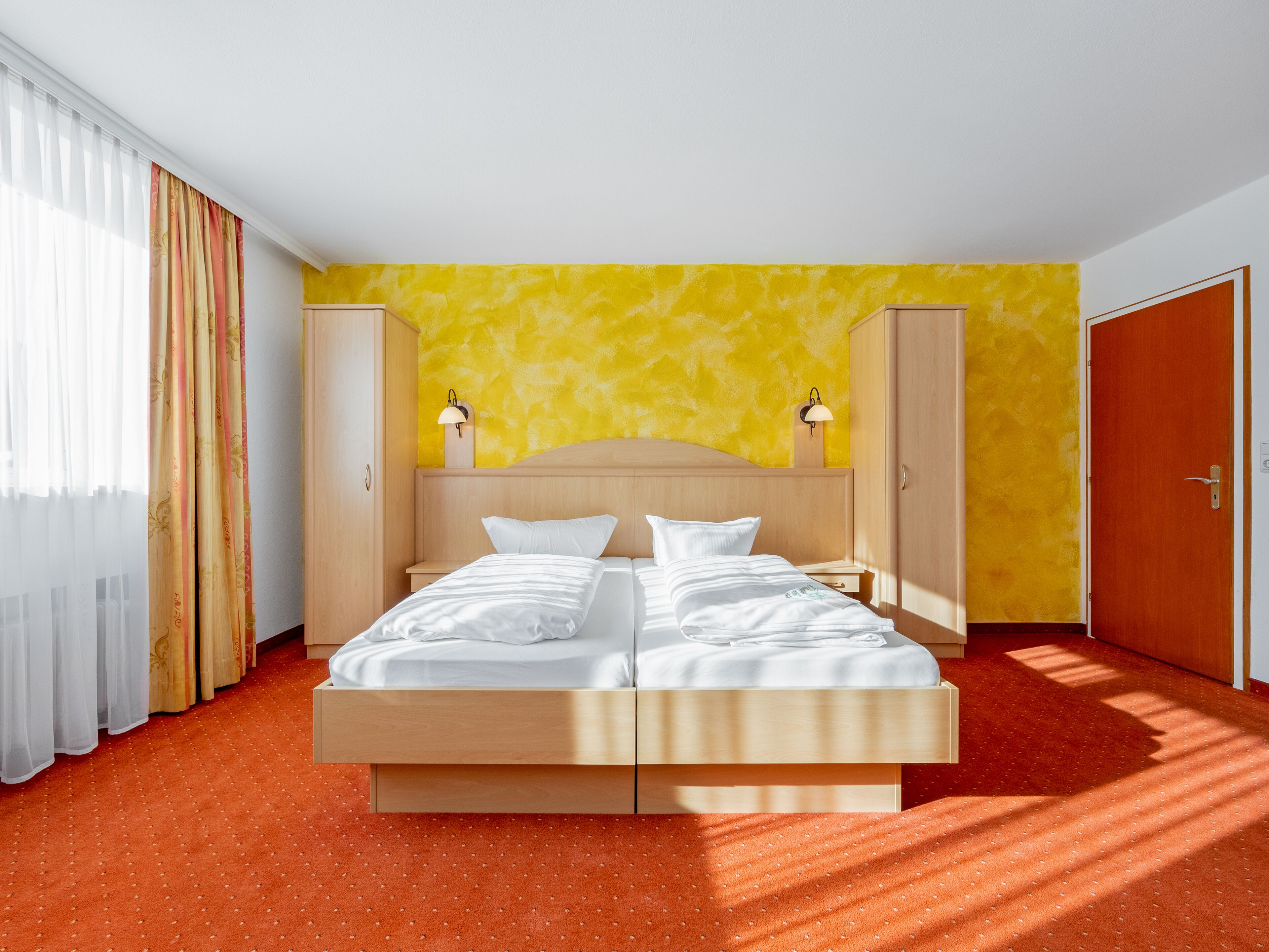 Una cama doble con cabecera de madera, dos mesitas de noche con lámparas, un armario y una puerta.