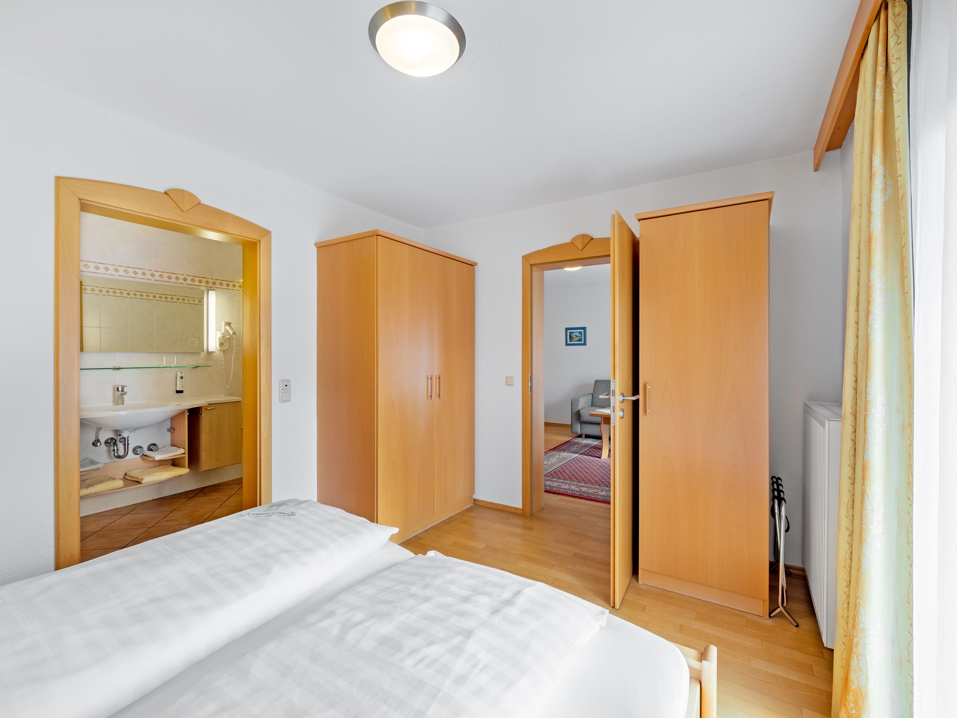 A bedroom with a bed, wooden wardrobe, and a bathroom with a mirror and sink.