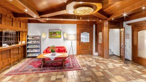 A wooden interior with a reception desk, a red sofa, a patterned rug, and a chandelier. - Landhotel Gabriele (Unterwoessen)