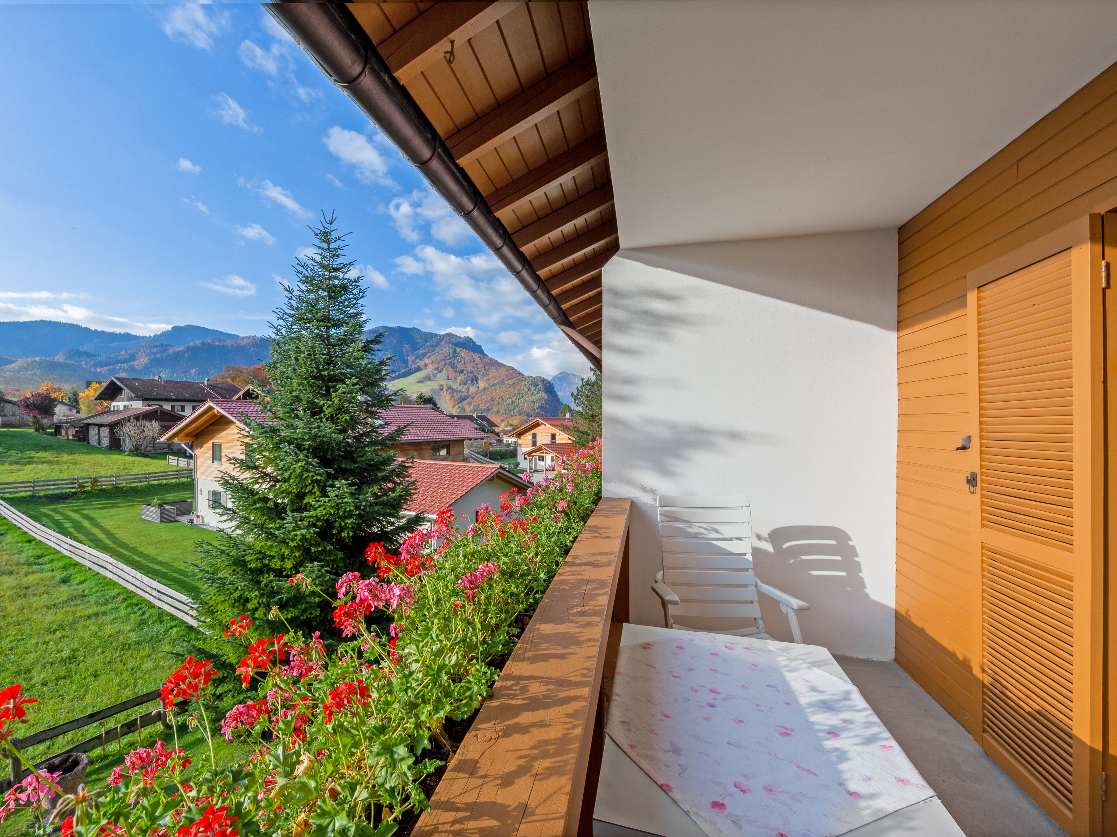 A balcony with a view of a mountain landscape, a wooden door, and a white chair.