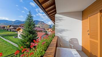 A balcony with a view of a mountain landscape, a wooden door, and a white chair.