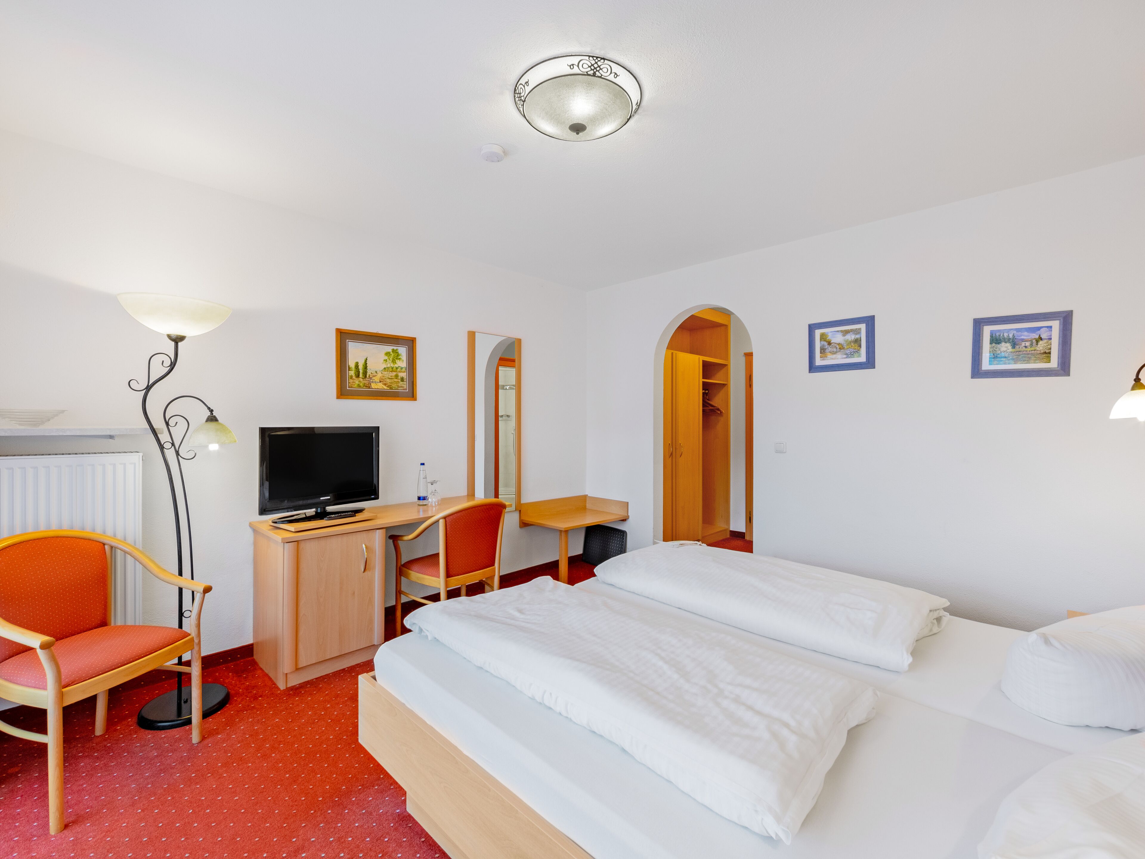 Une chambre d’hôtel comprenant un lit, un bureau avec un ordinateur, une chaise, une télévision, une lampe et une armoire.