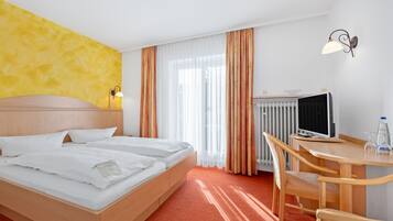 A hotel room with a bed, a desk with a computer, a chair, and a radiator.