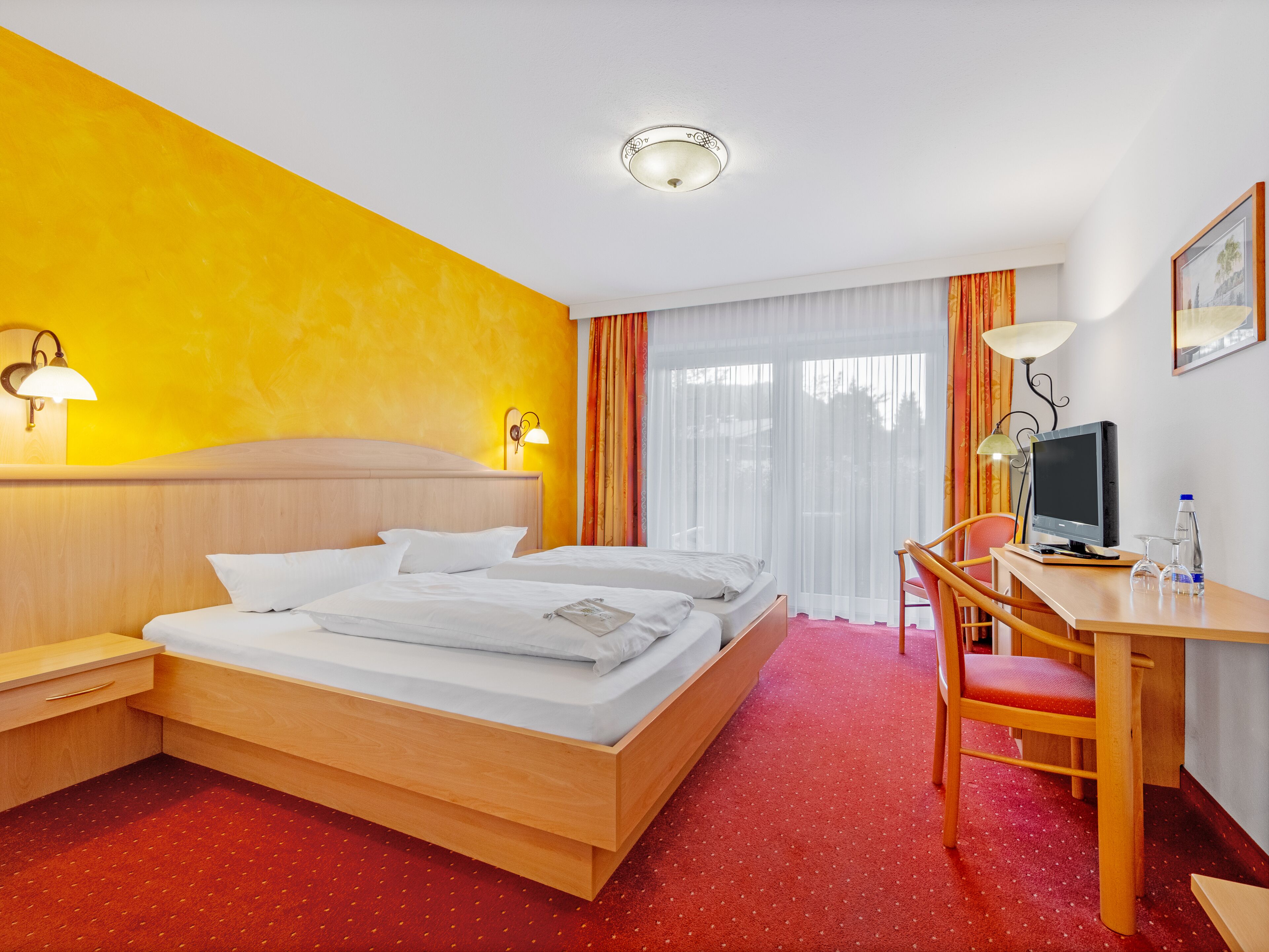 Een hotelkamer met een bed, een bureau met een computer, een stoel en een raam met gordijnen.