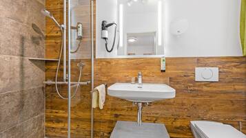 A modern bathroom with a glass shower enclosure, a white sink, and a toilet.