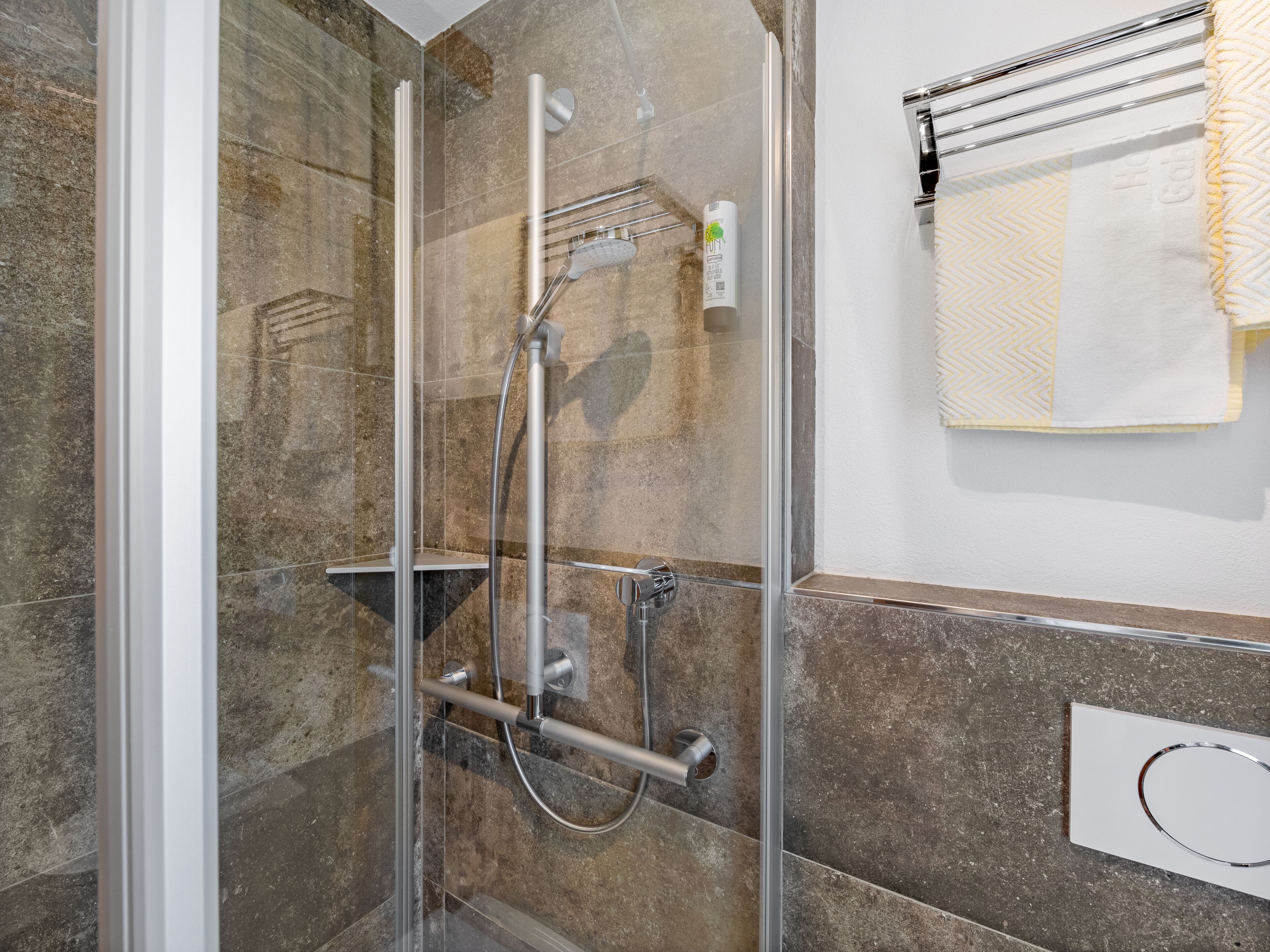 Ducha envuelta en vidrio con cabezal de ducha de mano y panel de control en la pared.