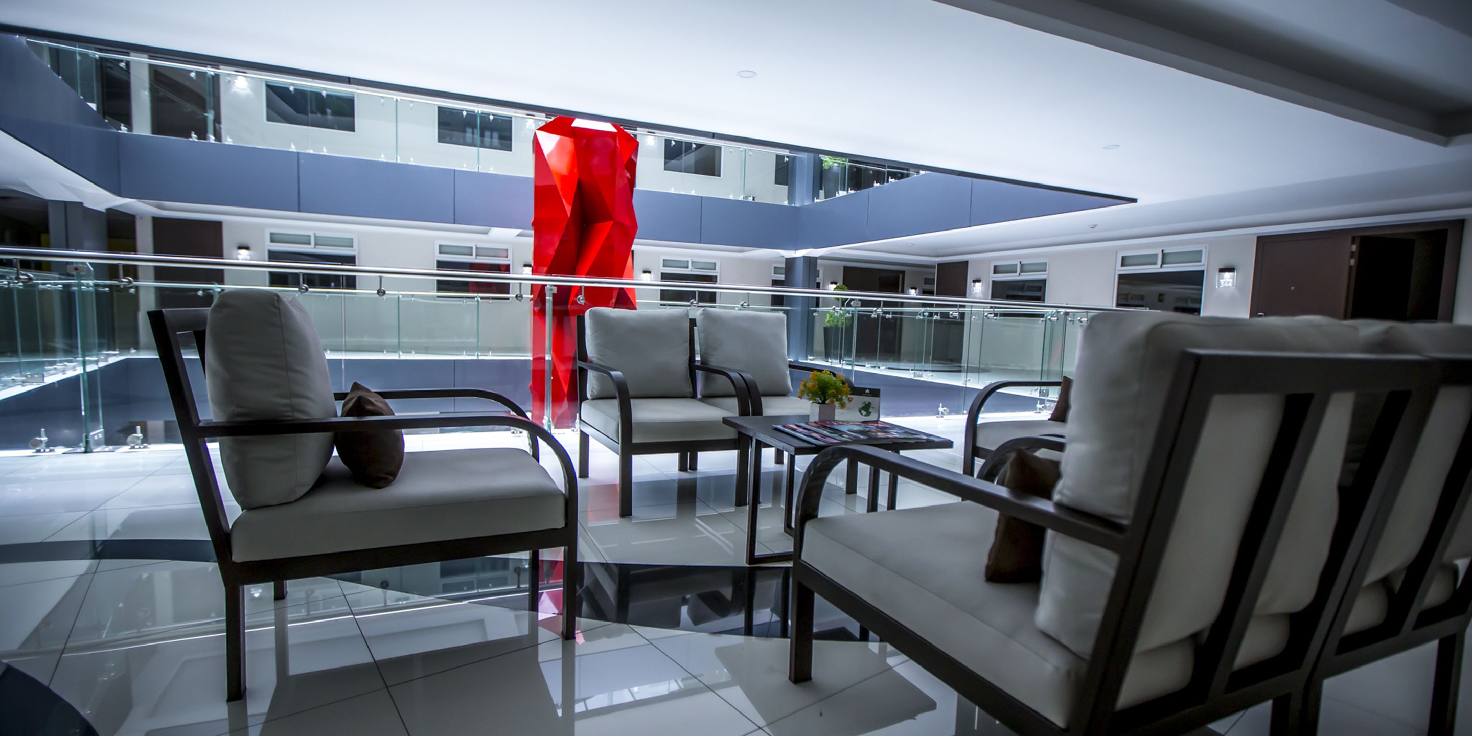 A modern hotel lobby with a glass railing, multiple seating areas, and a red sculpture.