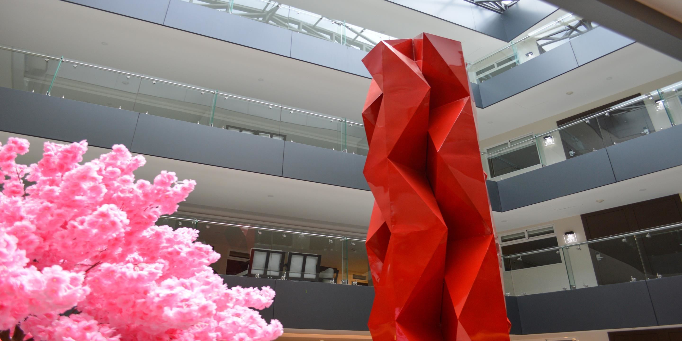 A modern interior with a geometric red sculpture, glass railings, and a pink flowering tree.
