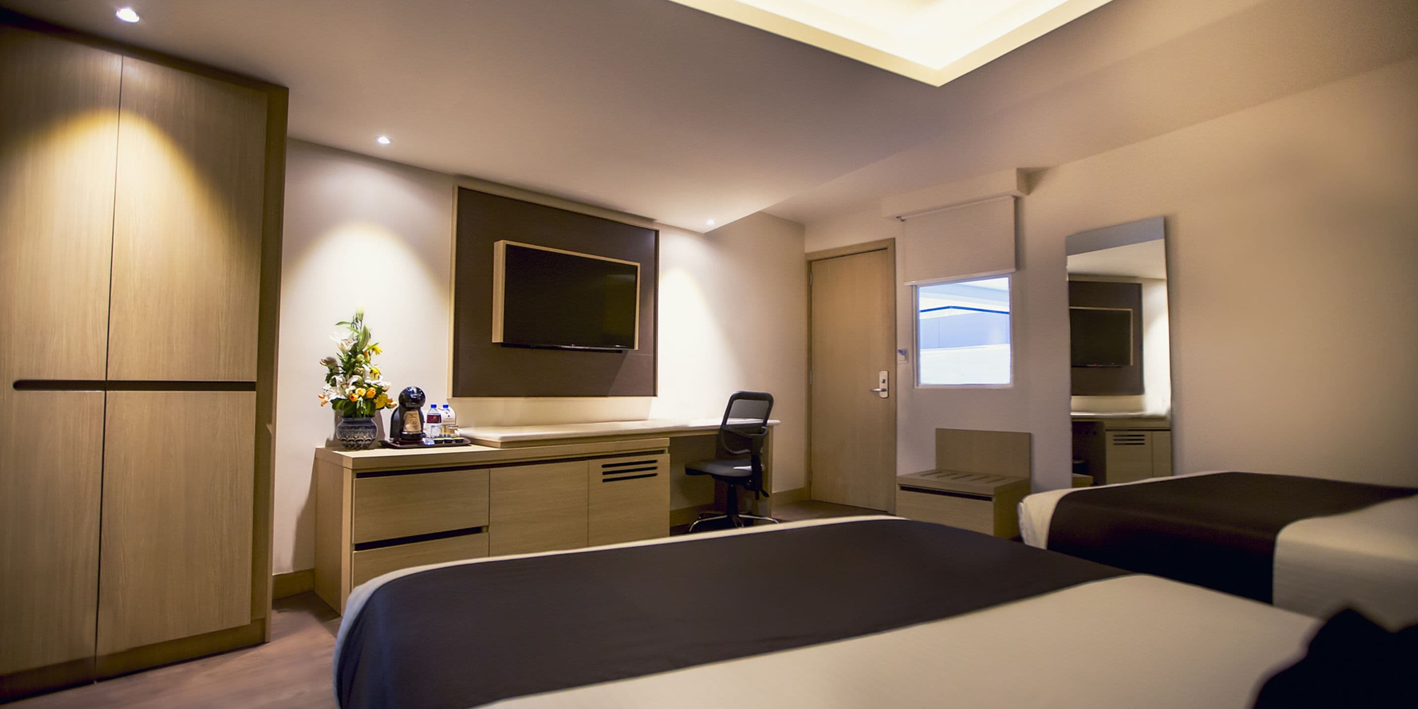 Una habitación de hotel moderna con cama, escritorio, silla y un espejo grande.