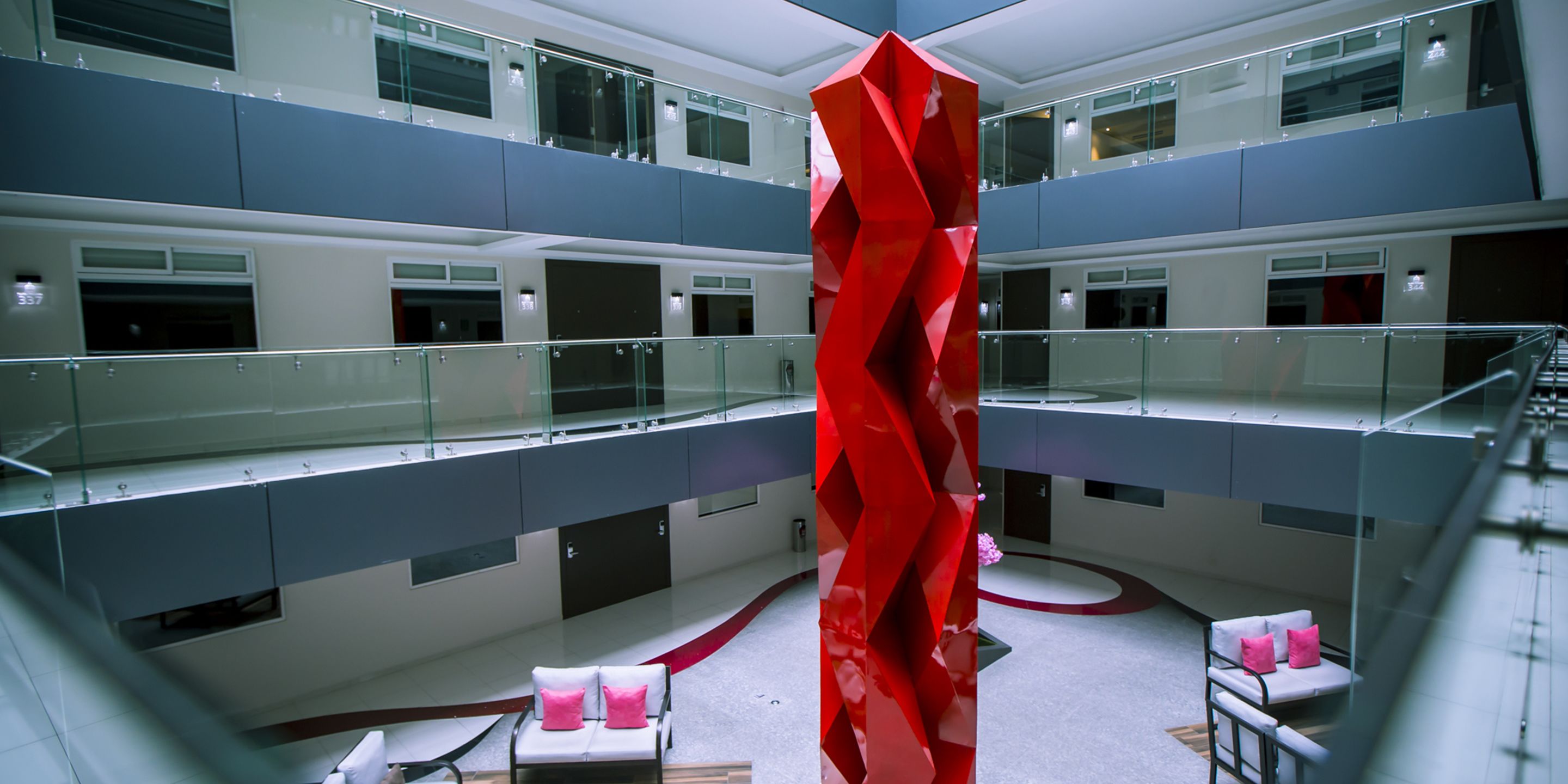Un atrio de varios niveles con una escultura roja central, barandales de vidrio y zonas de estar.