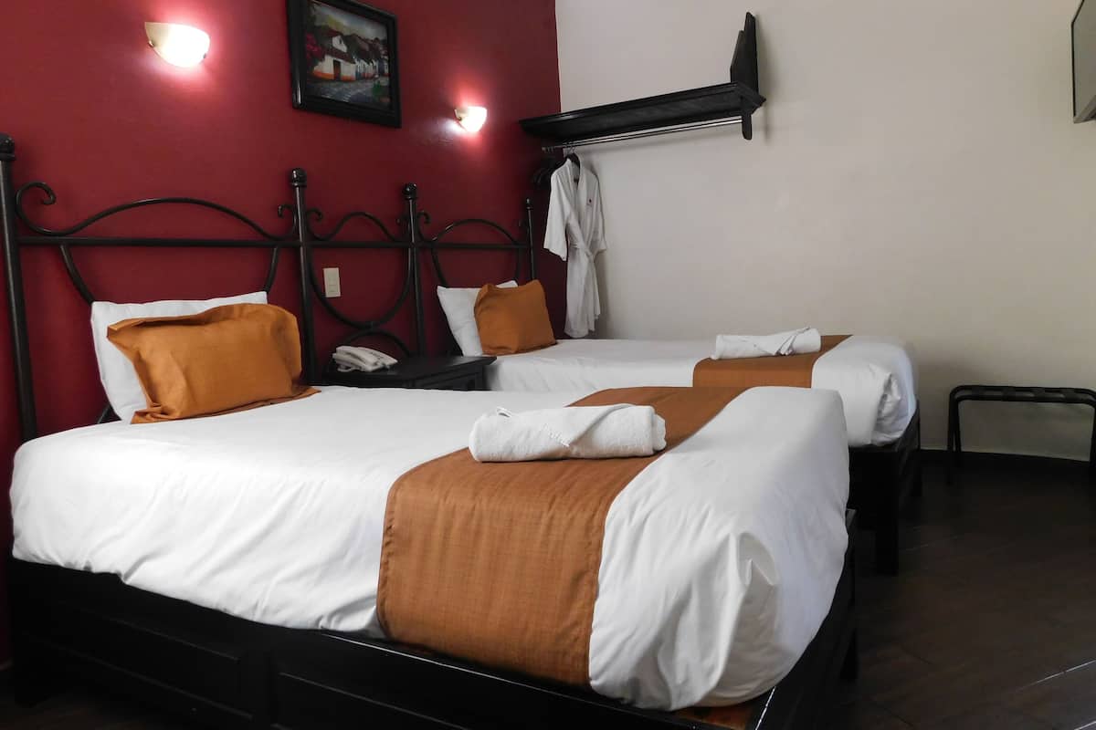 A hotel room with two beds, red walls, and a painting.