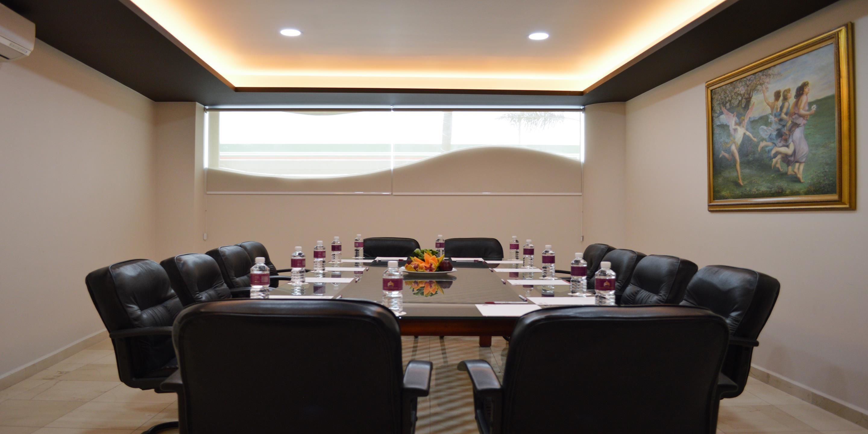 A conference room with a long table, black leather chairs, water bottles, and a painting on the wall.
