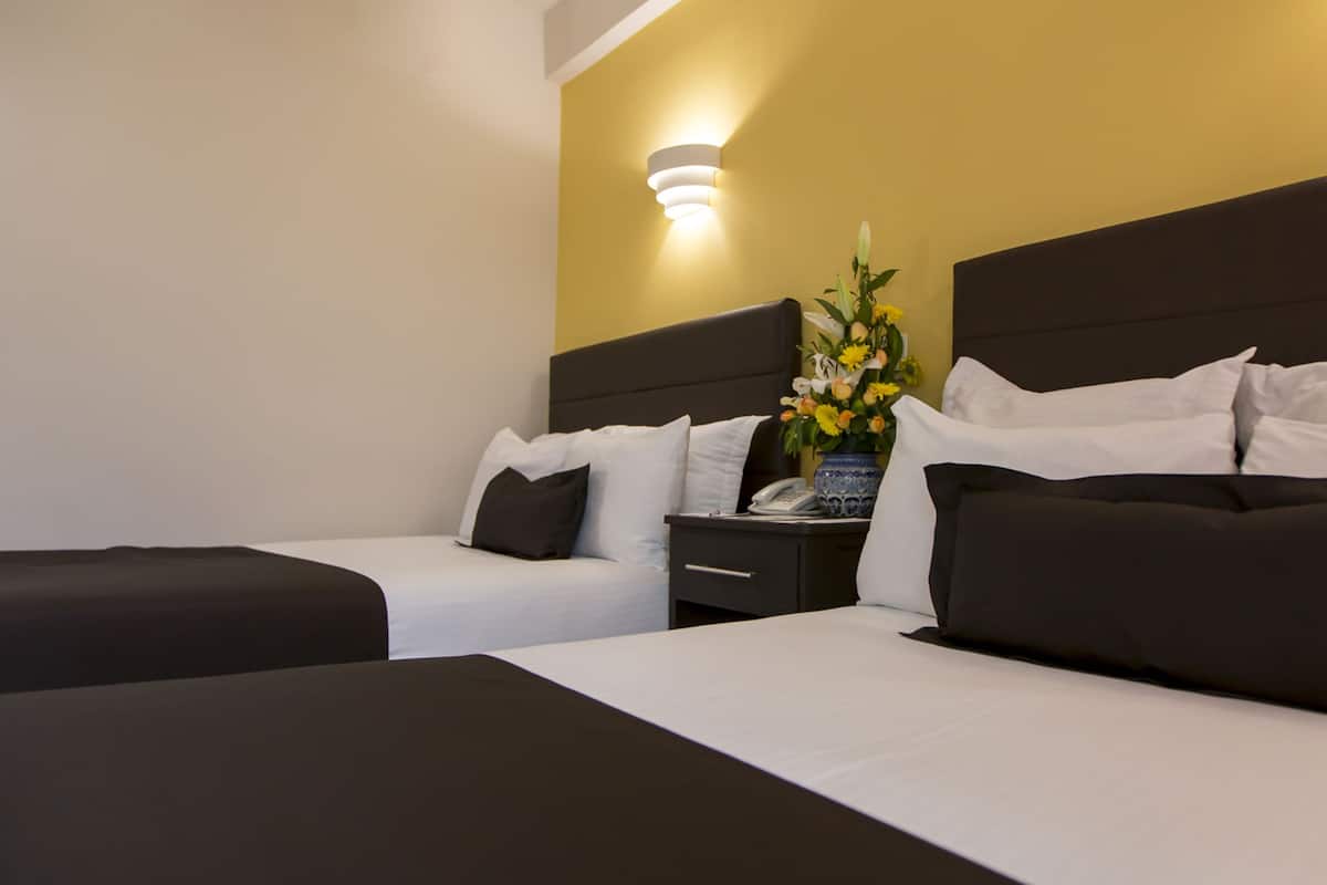 A hotel room with two beds, a nightstand with a phone, and a vase of flowers.