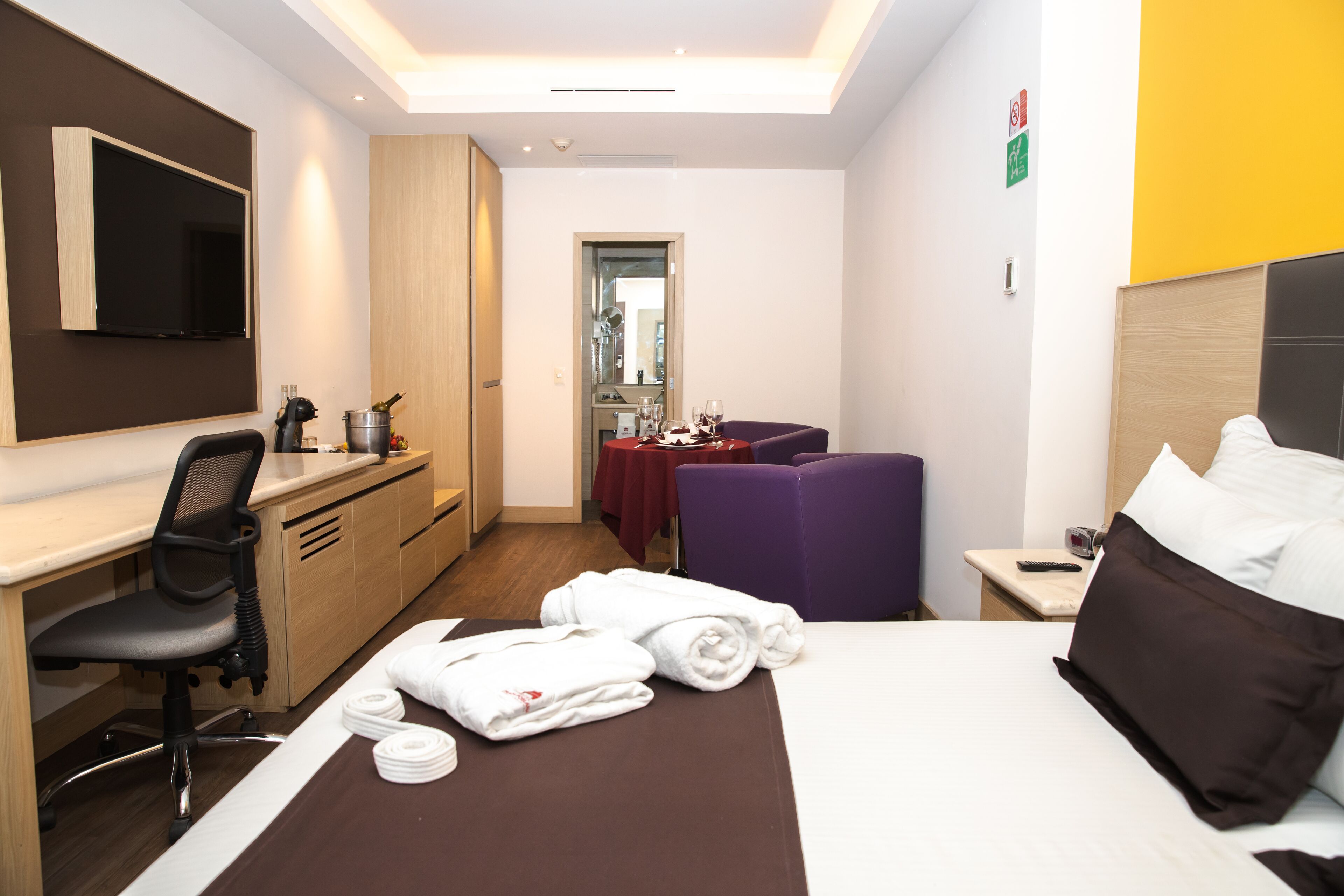 Une chambre d’hôtel avec un lit, un bureau, une chaise, une télévision et une salle de bain visible à travers une porte.