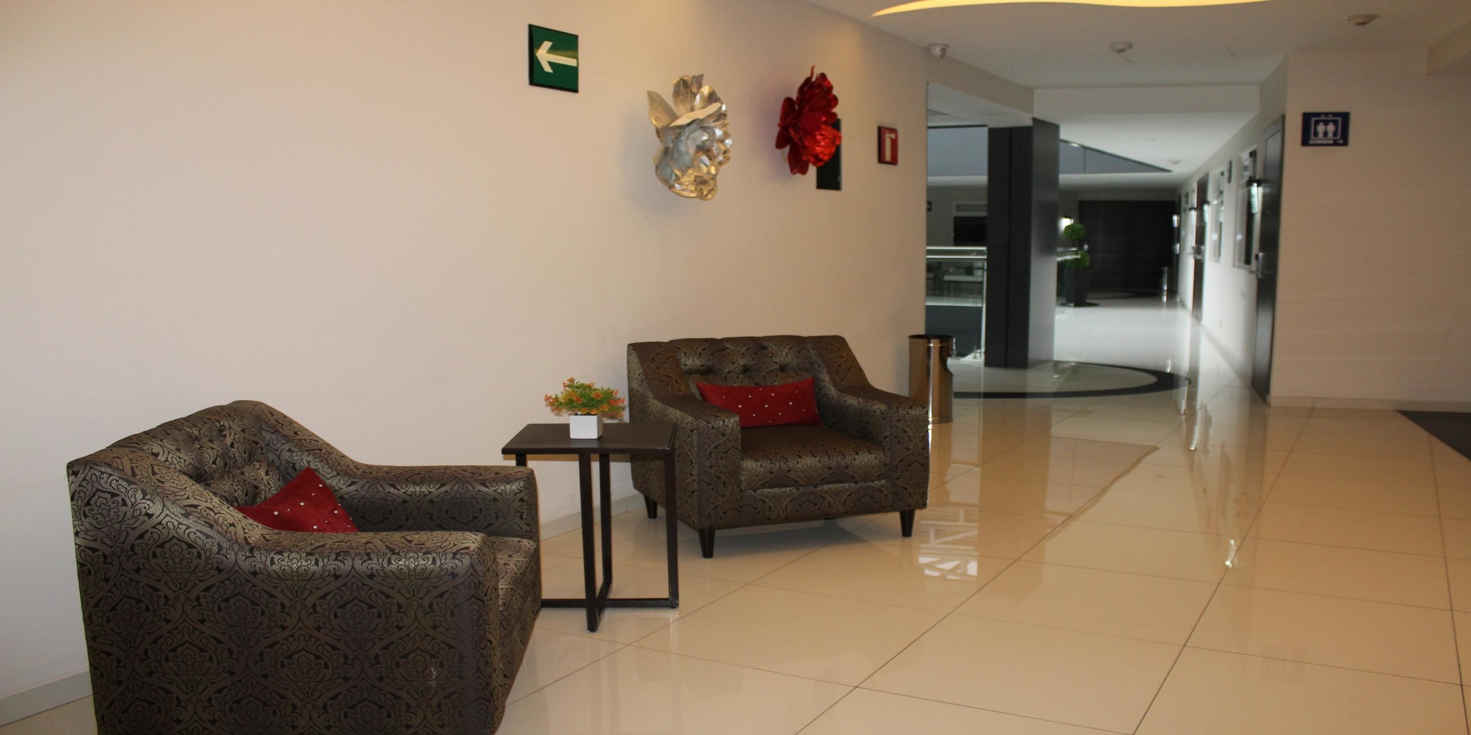 Eine Lobby mit zwei gemusterten Sesseln, einem kleinen Tisch mit einer Vase und einem Wegweiser an der Wand.