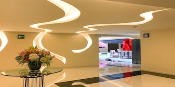 Een moderne lobby met een glazen tafel waarop een bloemstuk, een routebord en een bordje voor de toiletten staan.