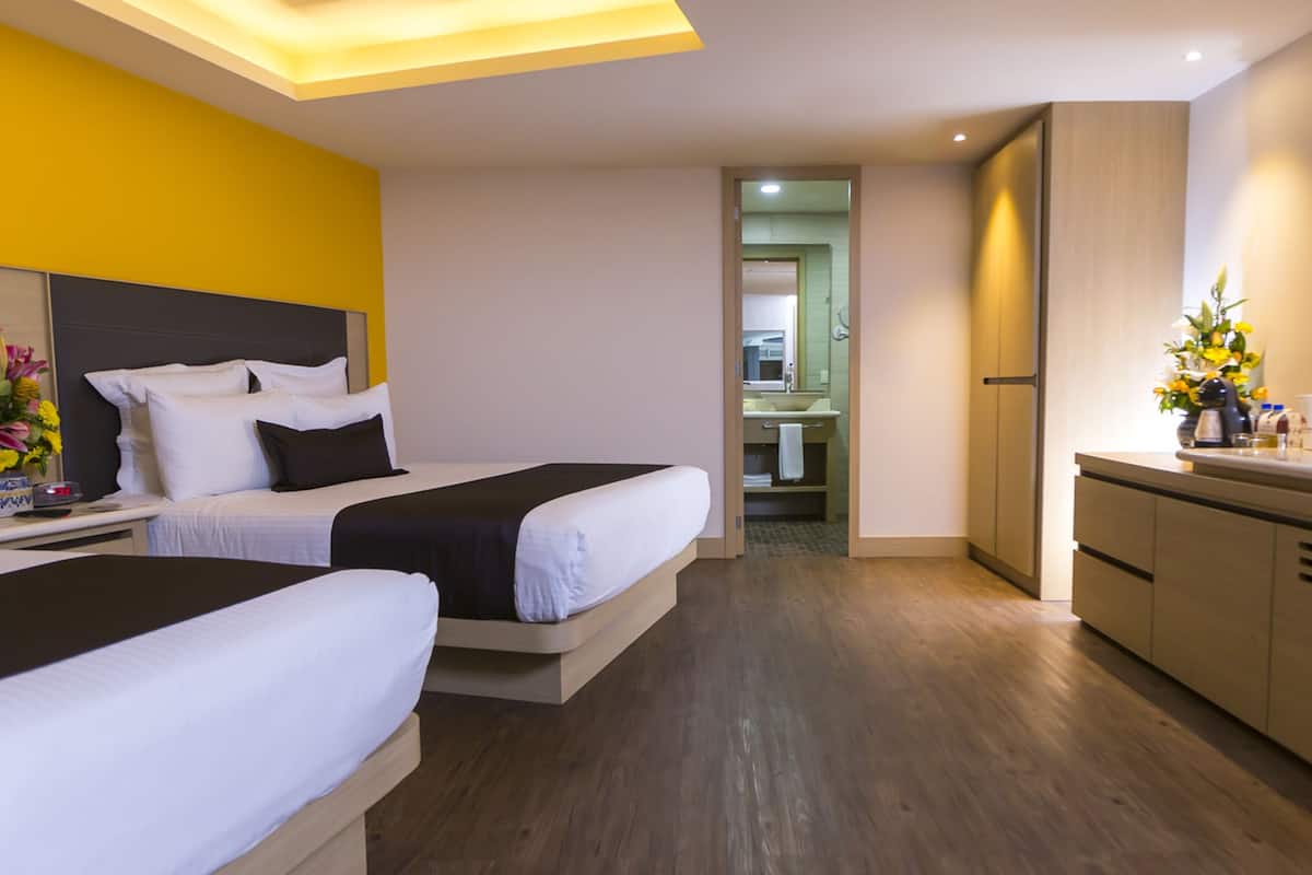 A hotel room with two beds, a small kitchenette, and a bathroom visible through an open door.