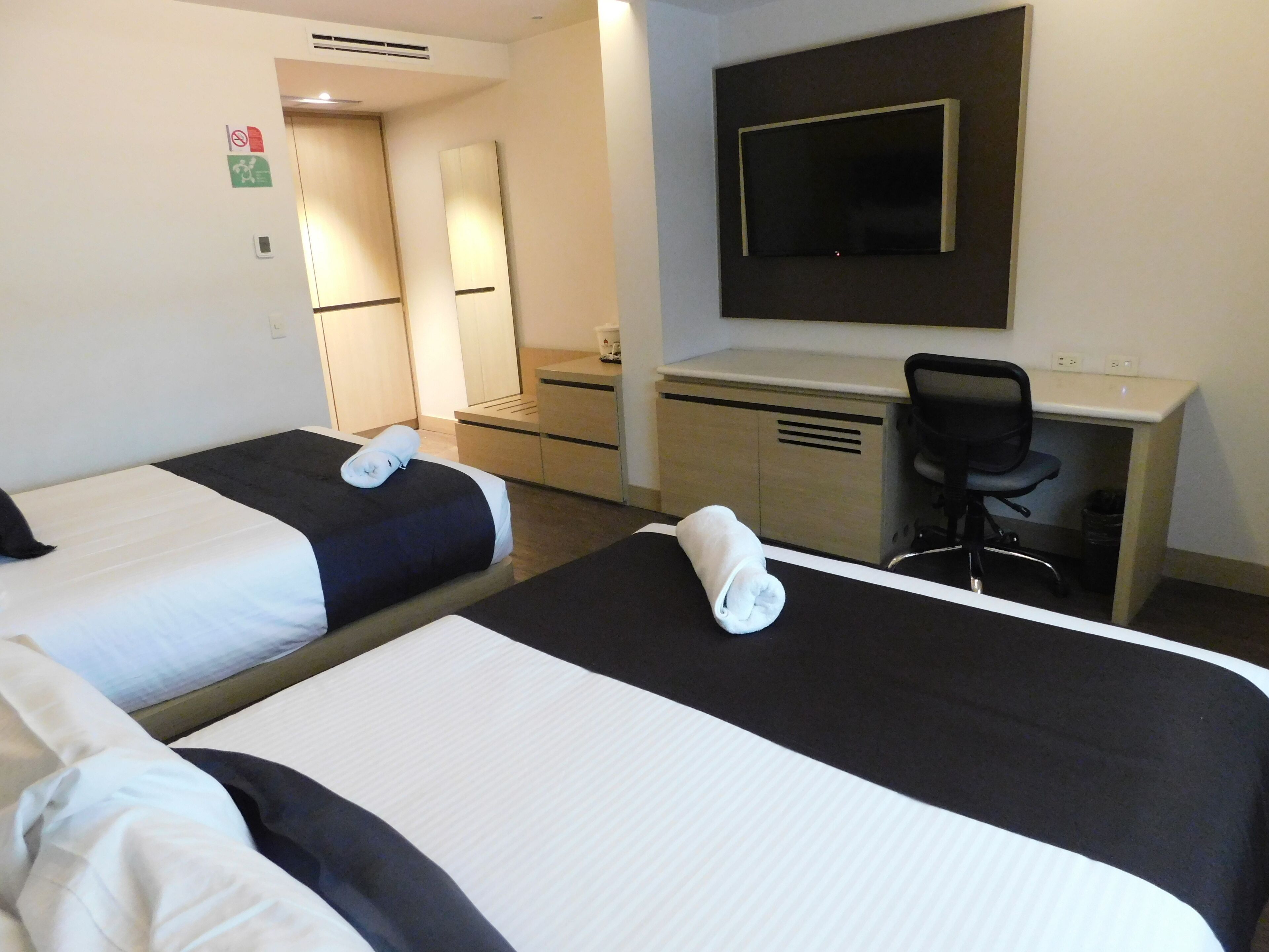 Una habitación de hotel con dos camas, un escritorio, una silla y un televisor montado en la pared.