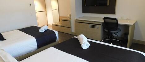 Una habitación de hotel con dos camas, un escritorio, una silla y un televisor montado en la pared.