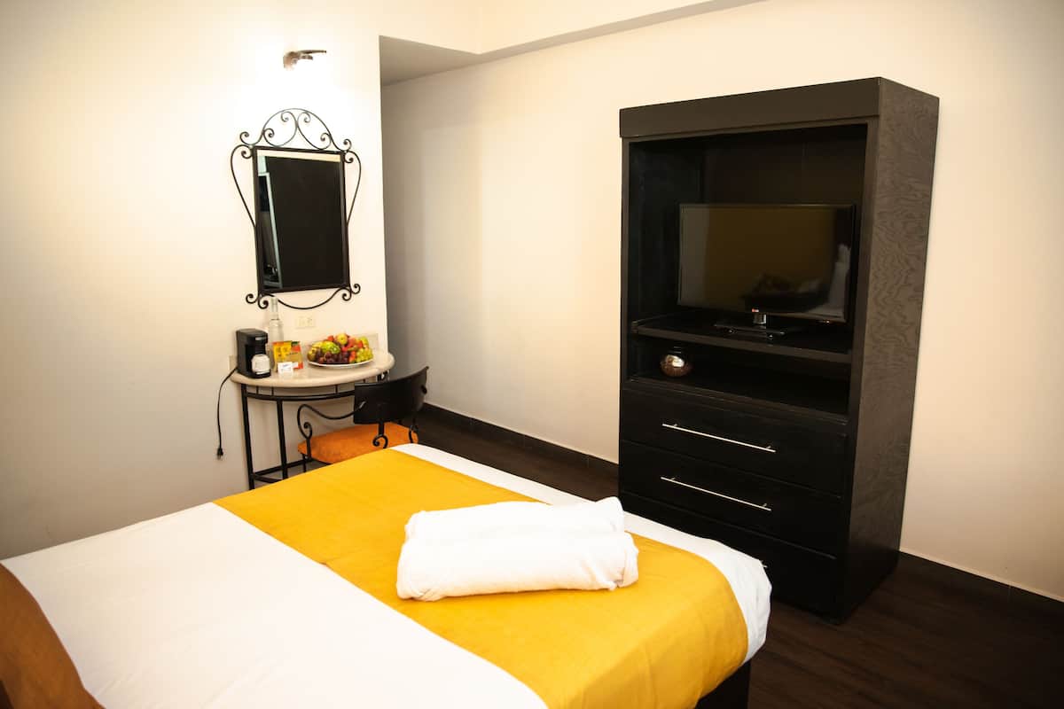 A hotel room with a bed, a desk, a chair, a TV, and a wardrobe.