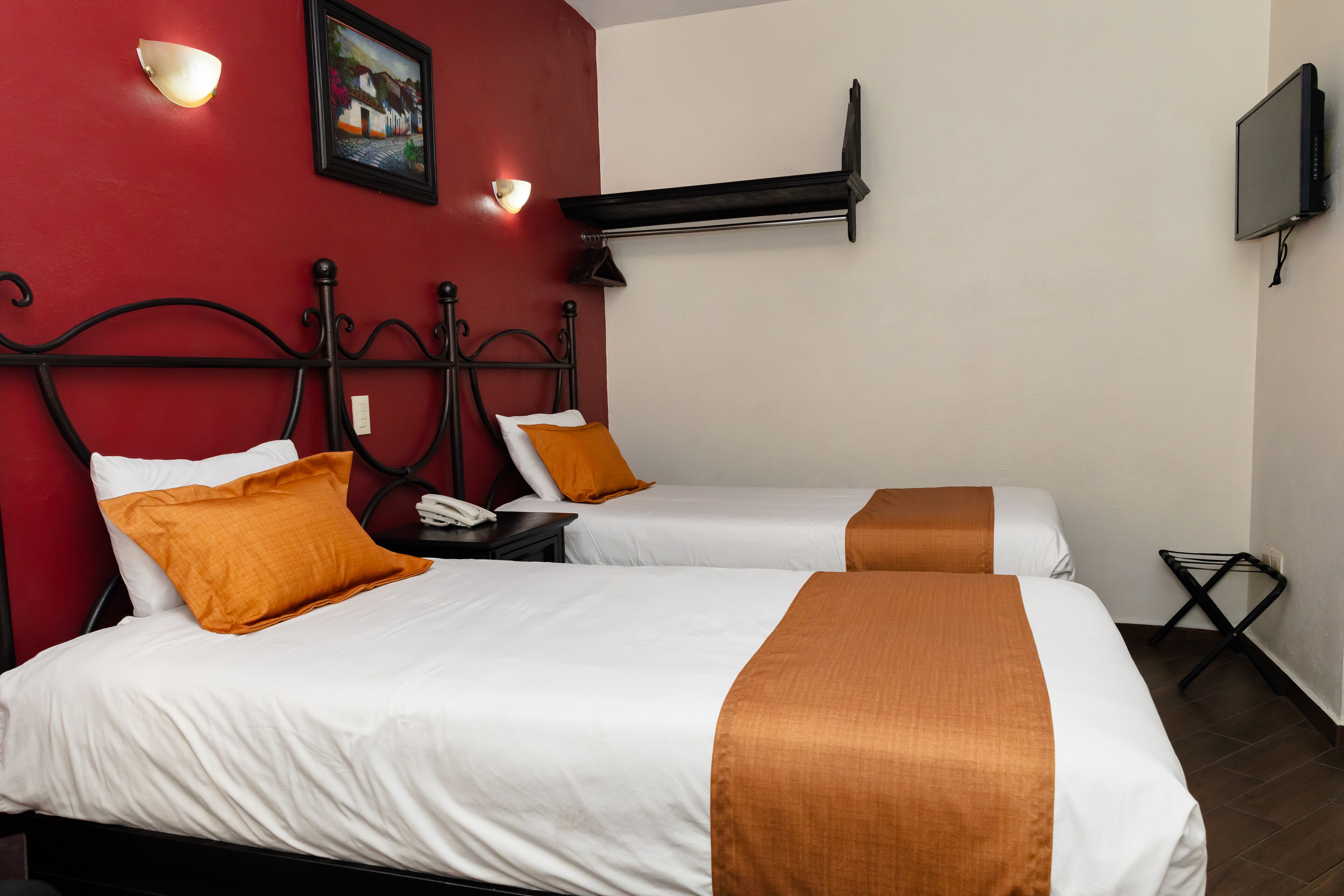 A hotel room with two beds, red walls, a painting, a TV, and a small table.