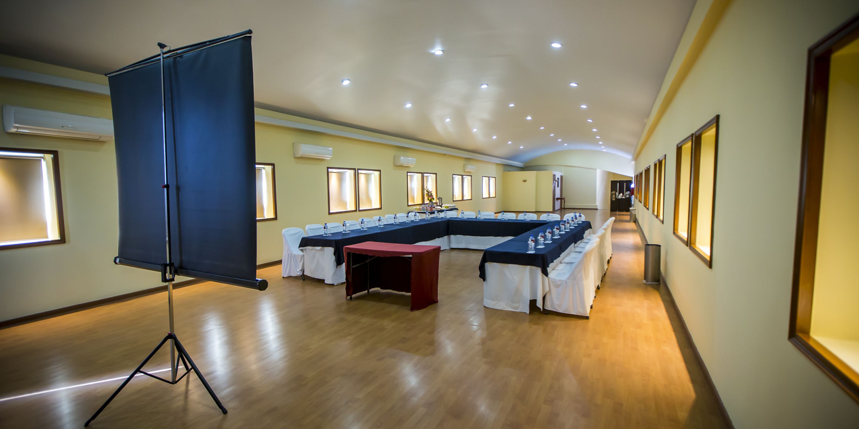 Ein Konferenzraum mit langem Tisch, weißen Stühlen und einer Projektionsleinwand.