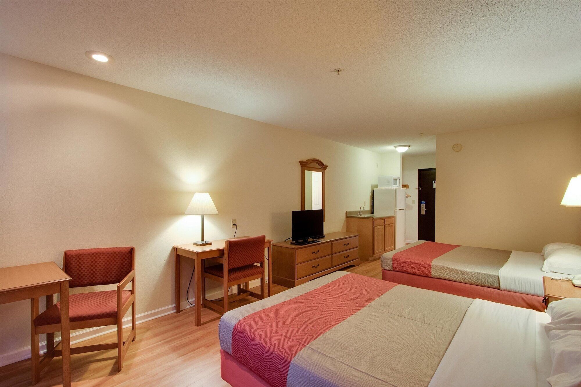 Habitación de hotel con dos camas, un escritorio, una silla, un televisor y un espejo.